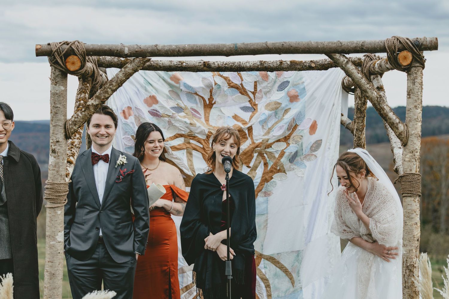 Wedding ceremony setup with rustic wooden arch and white fabric against fall foliage.