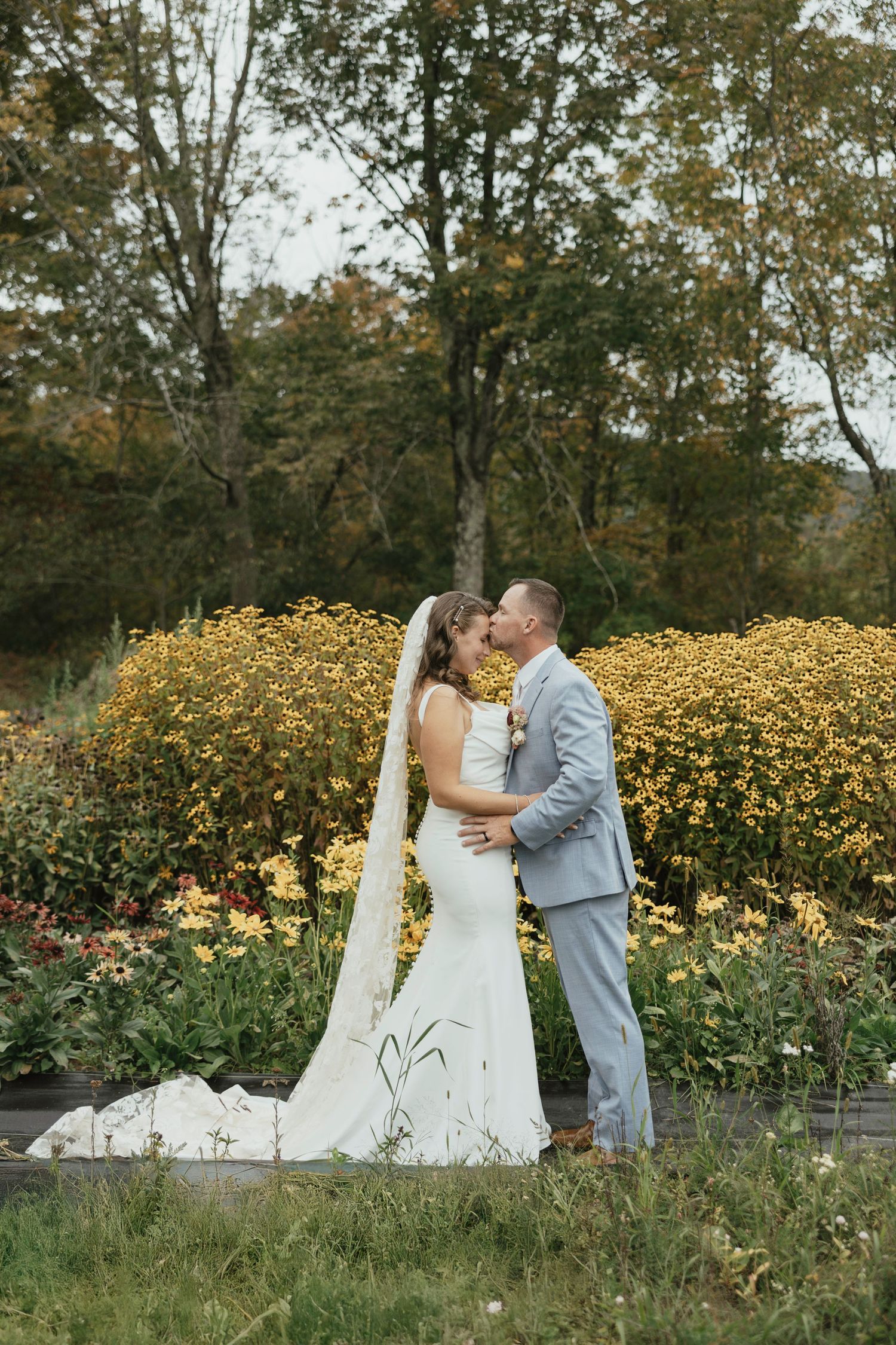 A romantic wedding moment captured in front of vibrant yellow wildflowers on a beautiful autumn day.
