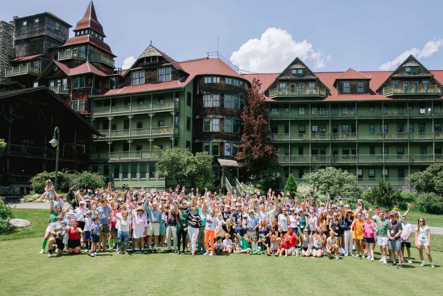 Large group of people gathered in front of a historic green hotel with Victorian architecture and white trim details.