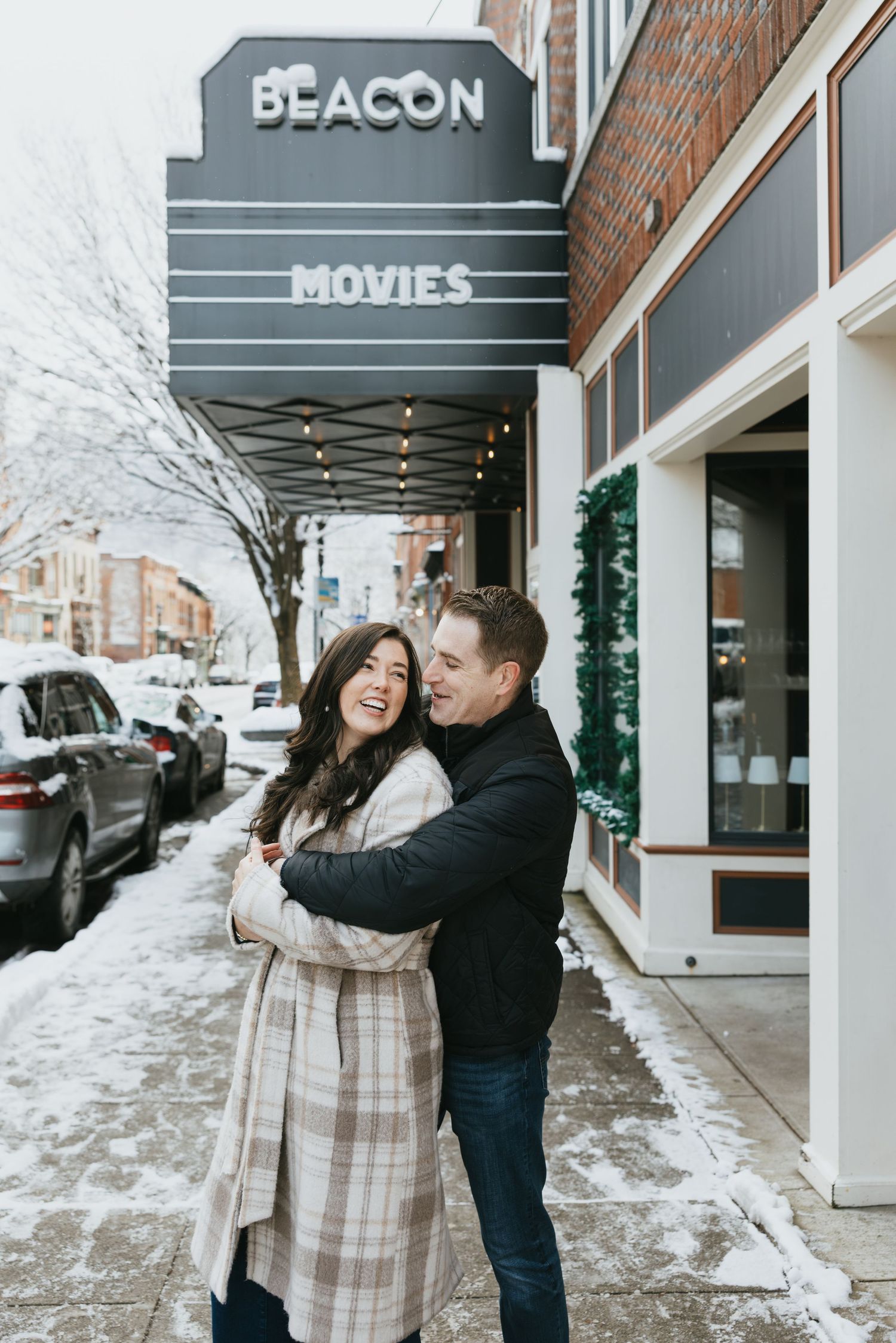 Couple embracing and laughing outside Beacon Movies theater on a snowy winter day.