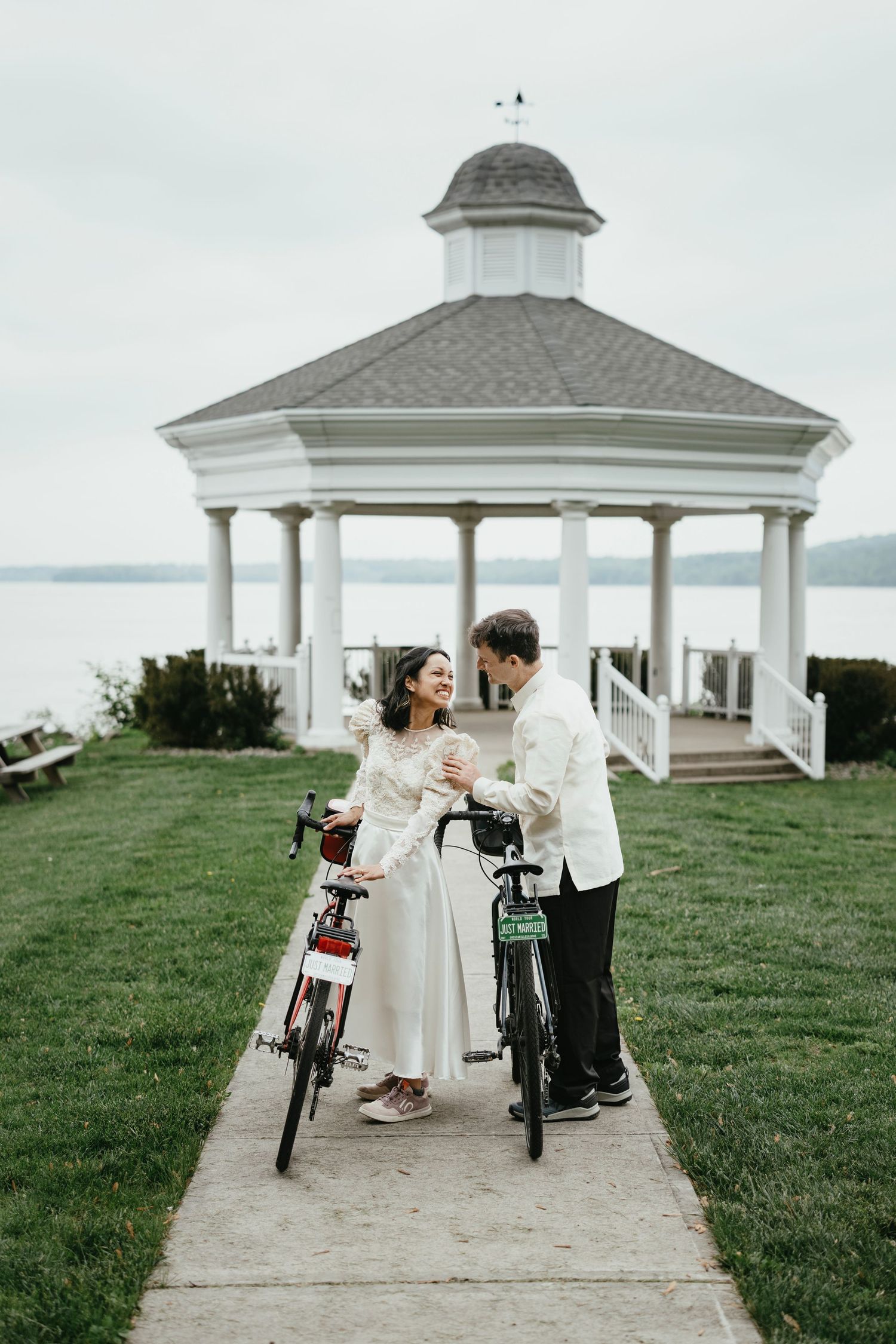 Two people share a romantic moment near a white gazebo with vintage bicycles parked beside them.