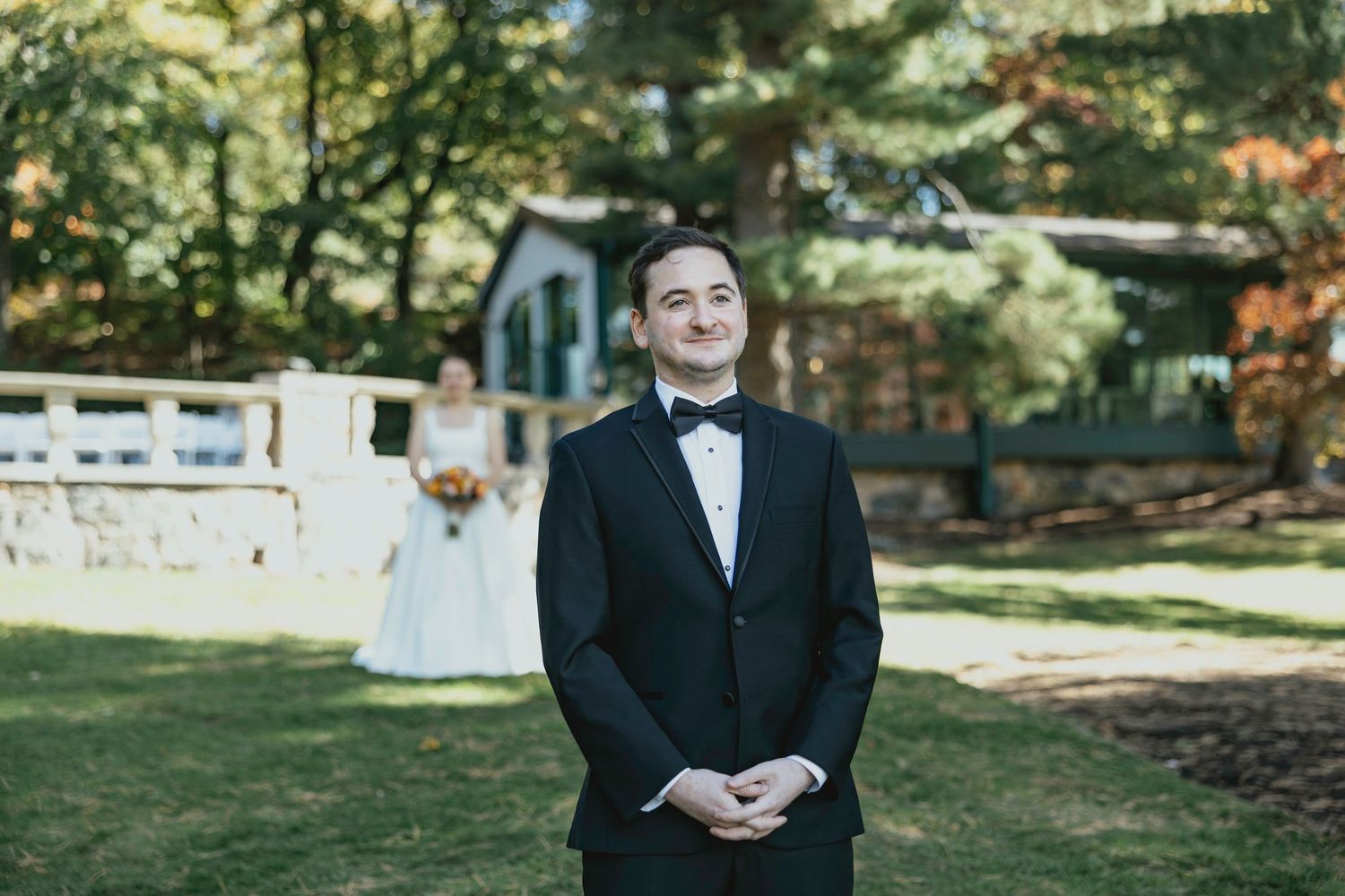 A person in a black tuxedo poses outdoors in a garden setting during a formal event.