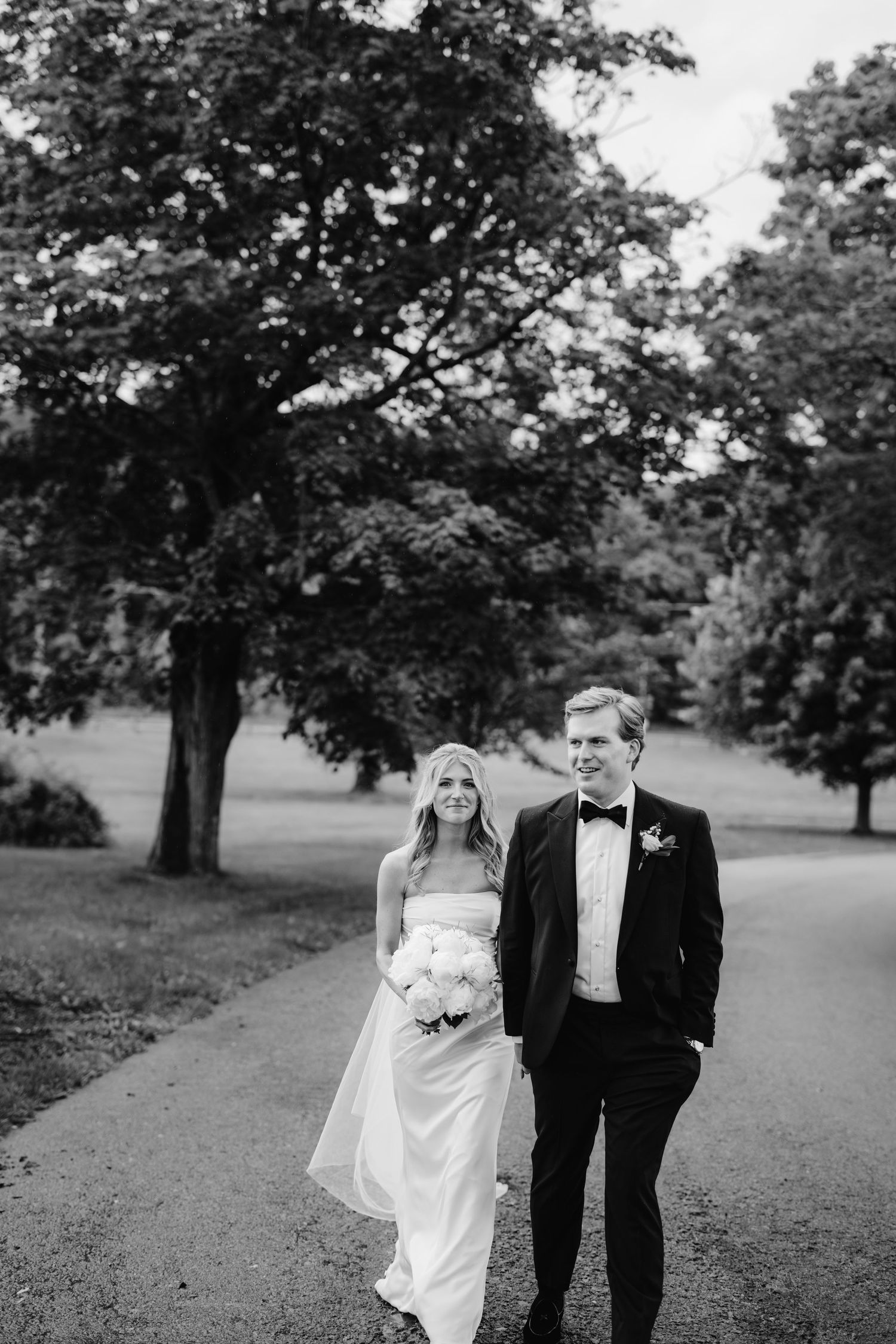 Black and white wedding photos of a couple walking together on a tree-lined path.