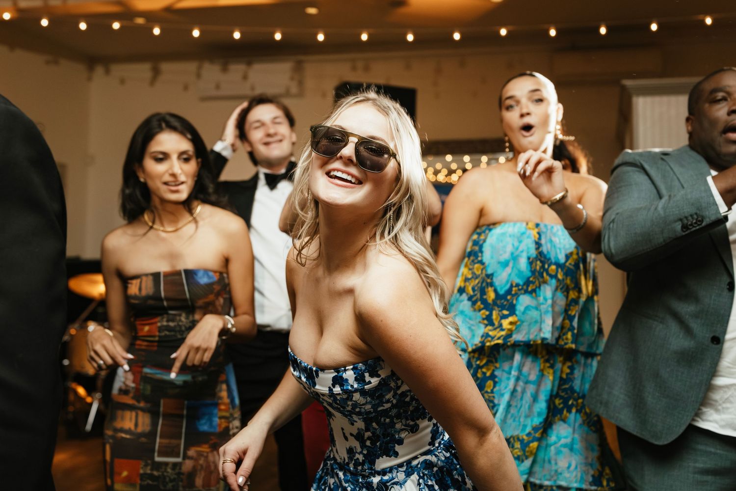 Wedding guests dancing together on a dance floor under string lights at an evening reception celebration.