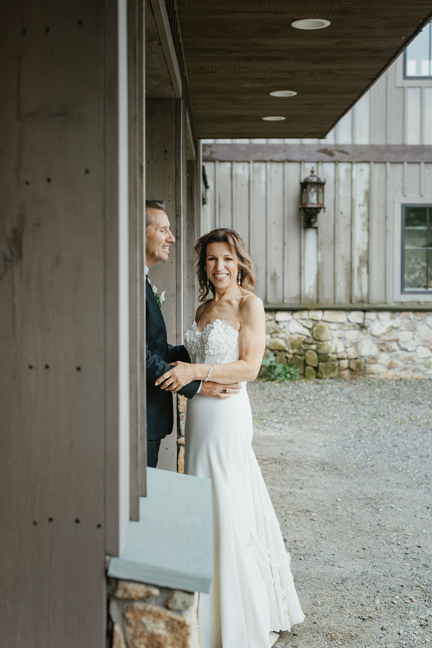 A bride in a white lace wedding dress poses gracefully under a covered porch area.