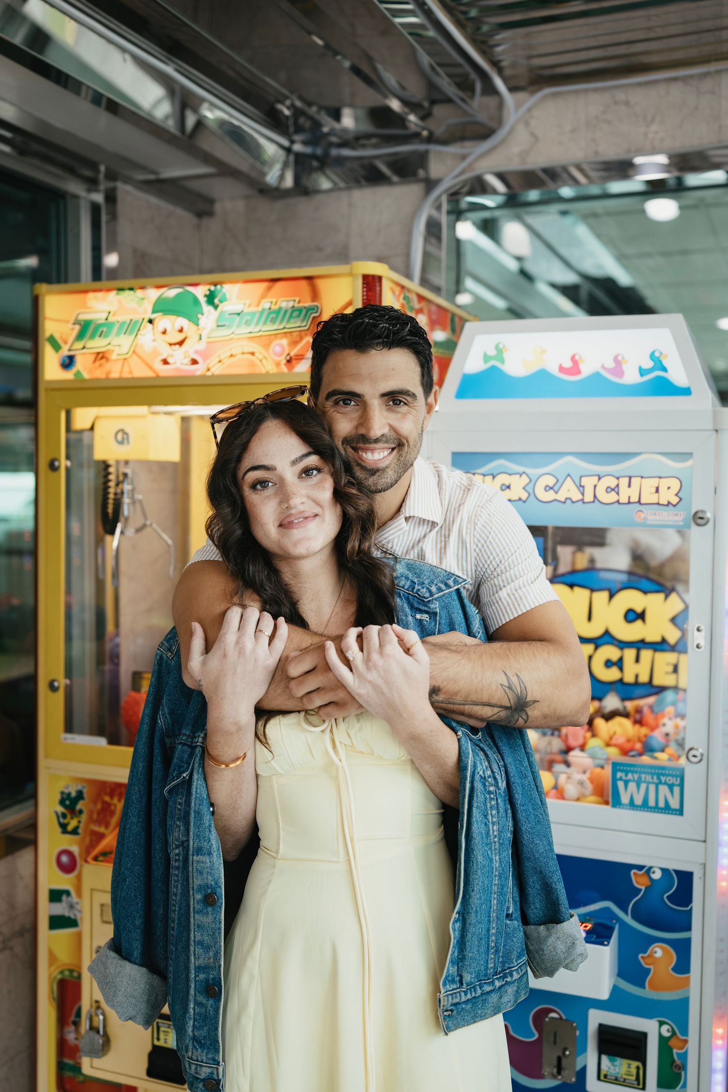 Couple posing playfully together in an arcade with vintage gaming machines and colorful signage in the background.