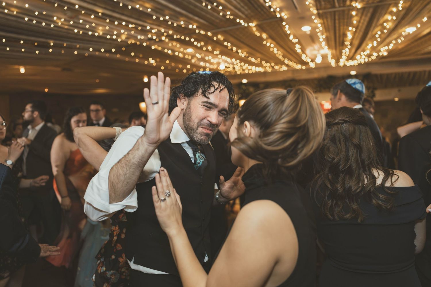 People dancing and celebrating at a wedding reception under twinkling string lights.