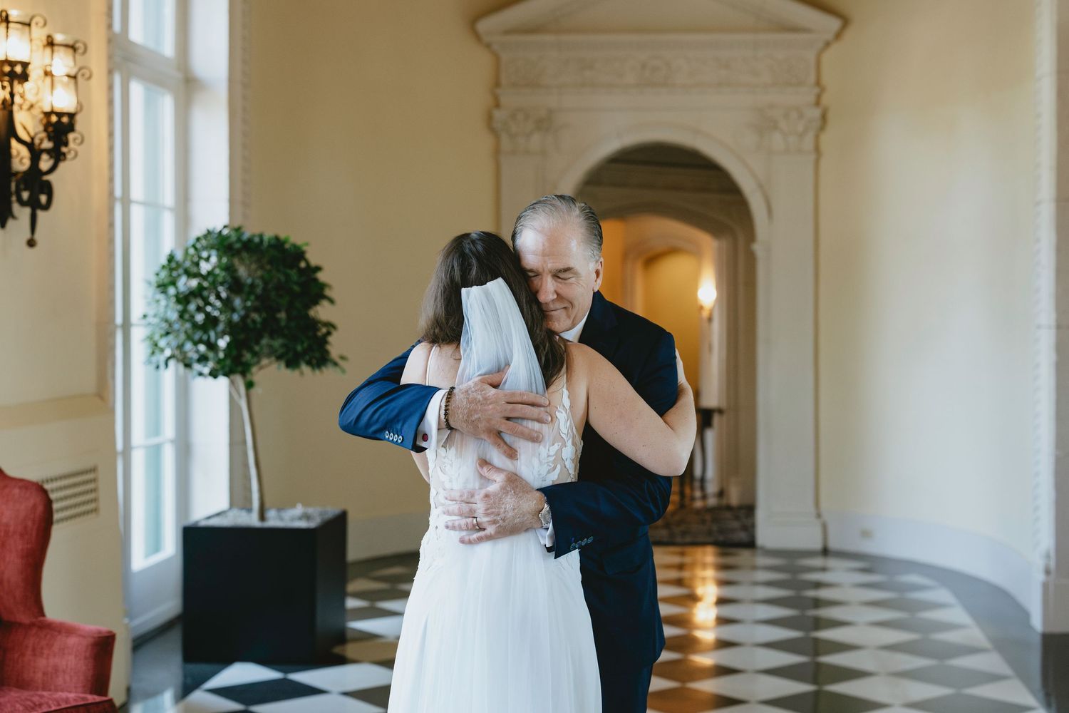 A romantic moment between a couple in formal attire dancing in an elegant white ballroom with ornate architecture.