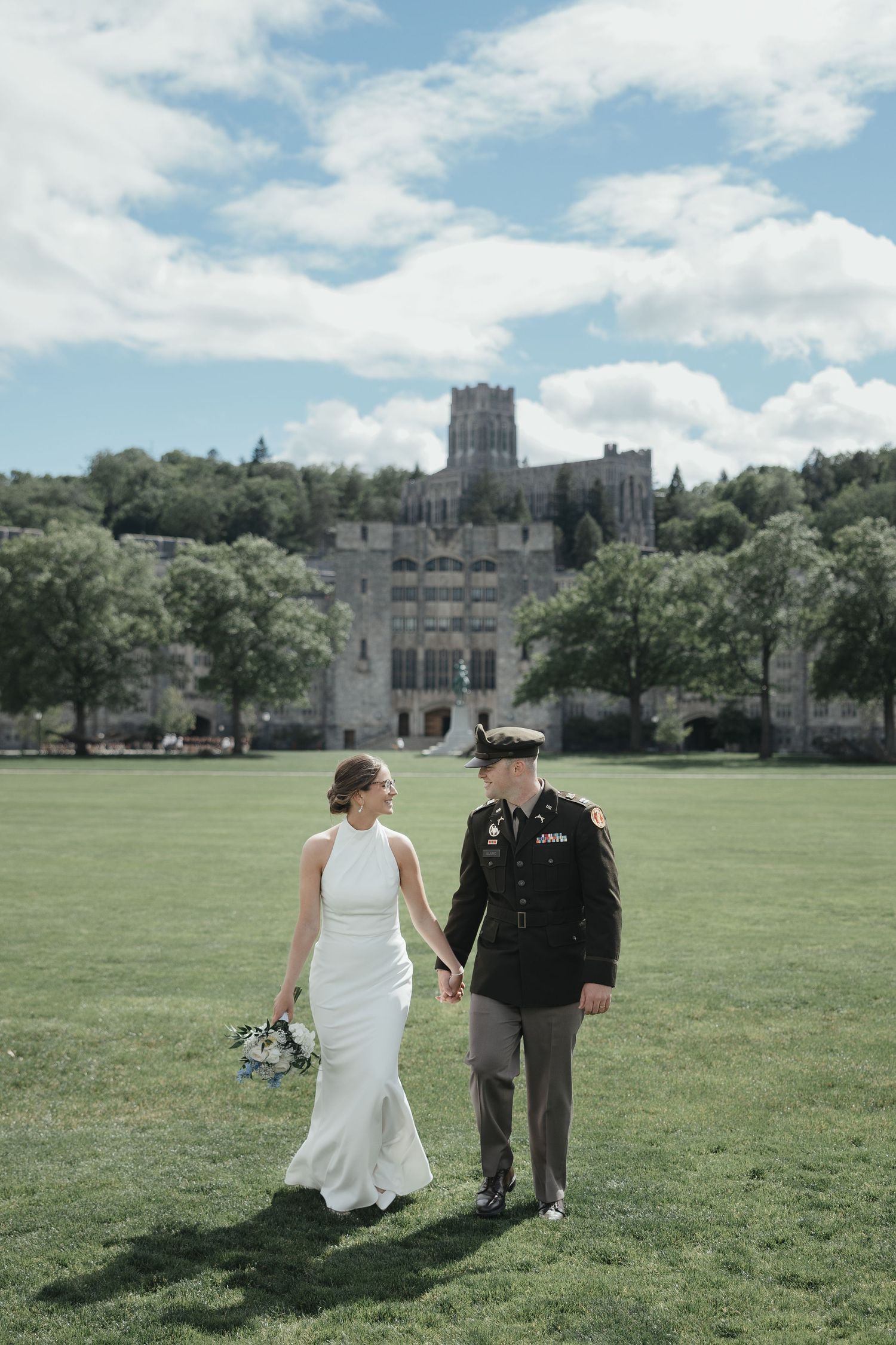 Bride and groom in military uniform hold hands walking on West Point Academy grounds on their wedding day.