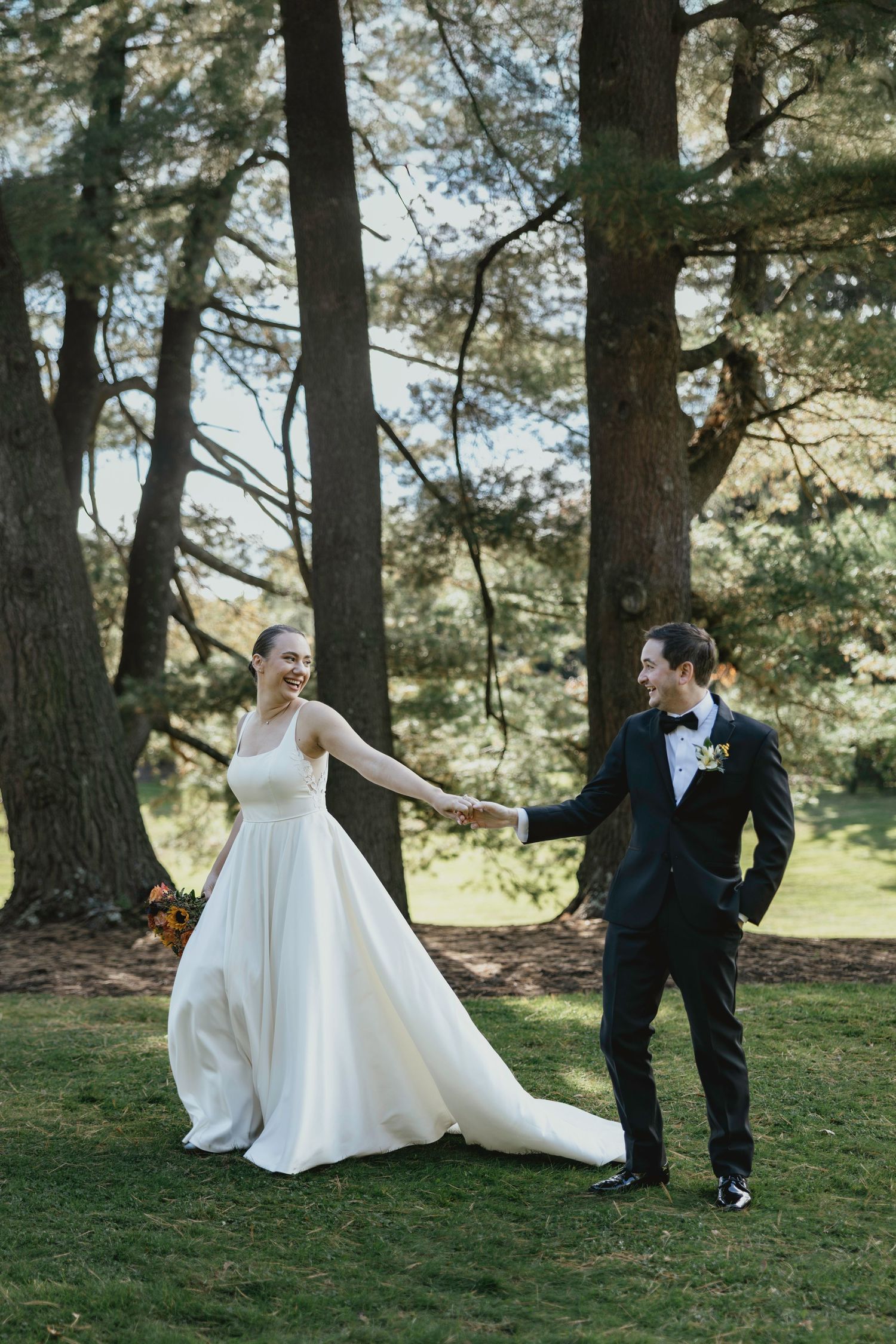 A wedding couple shares a playful moment together in a sun-dappled pine forest setting.