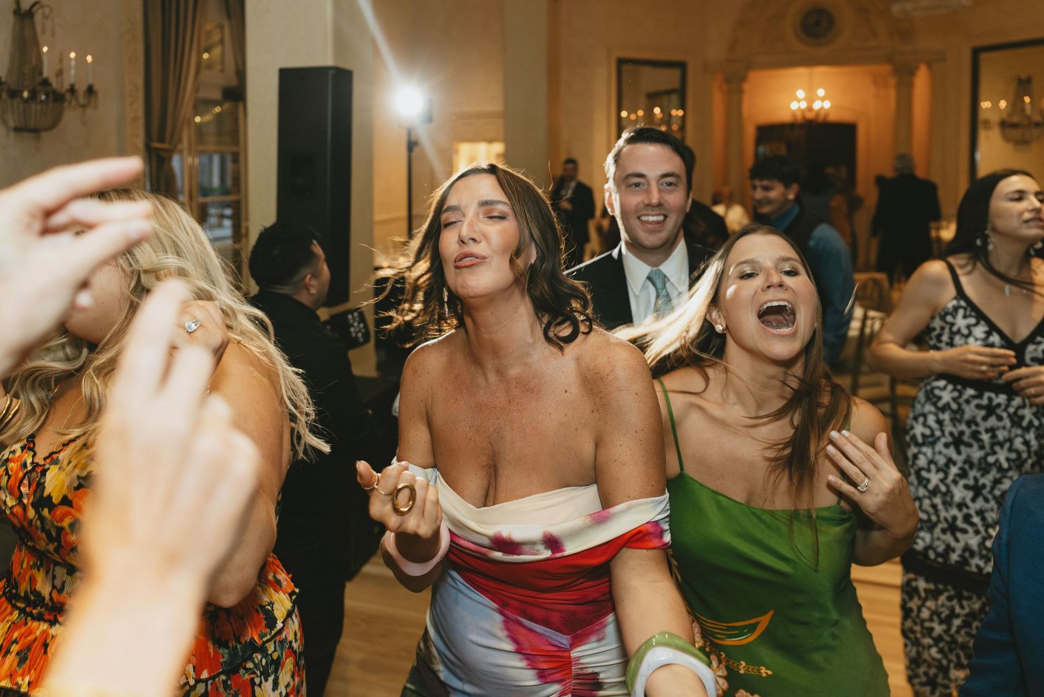 Wedding reception guests dancing and celebrating on a dimly lit dance floor with warm lighting.