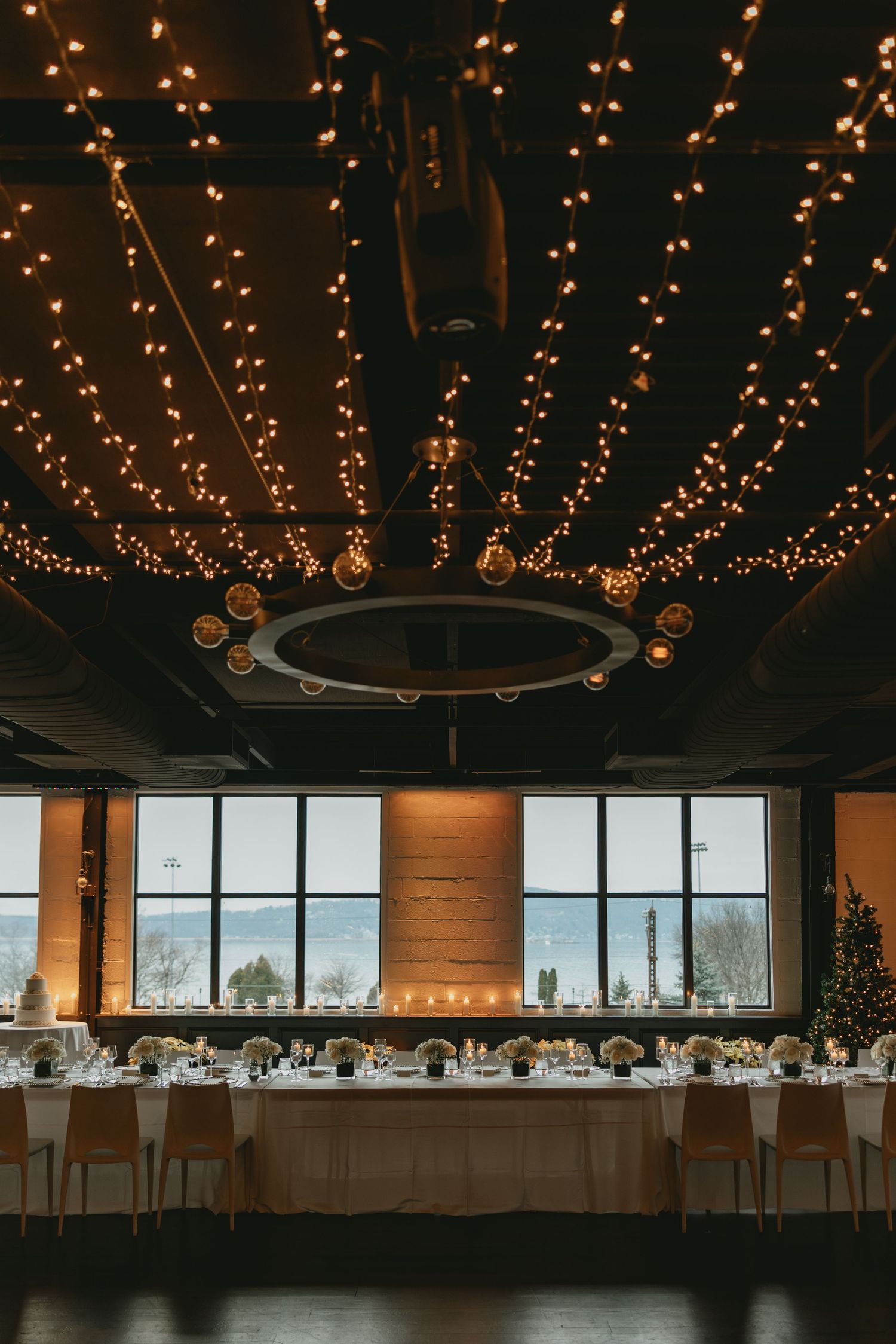 An elegant reception venue with string lights on the ceiling and large windows overlooking a scenic view.