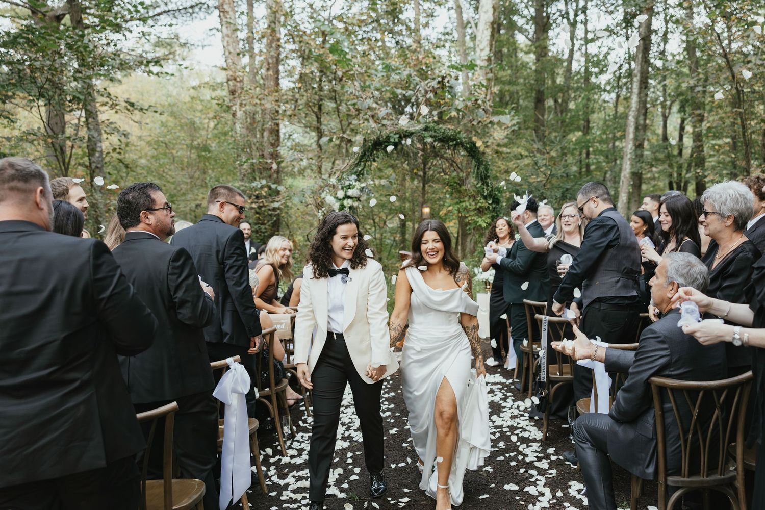 Wedding guests celebrate with confetti and sparklers during an outdoor forest ceremony.