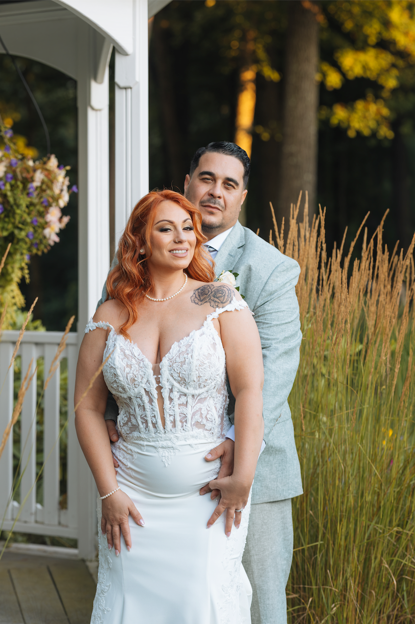 A couple poses together outdoors in front of tall ornamental grasses and autumn foliage.