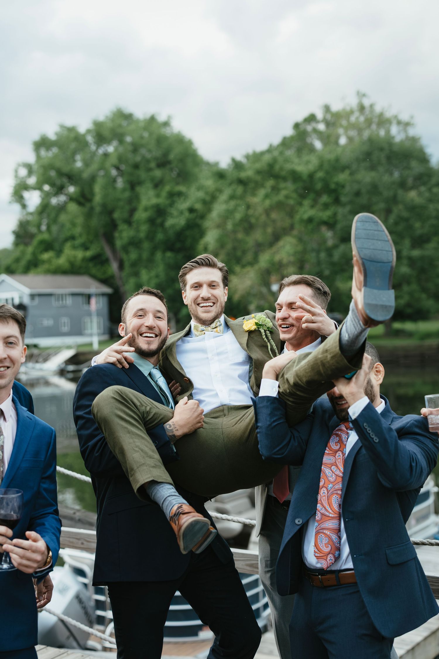 A group of groomsmen jumping and posing playfully outdoors during a wedding celebration.