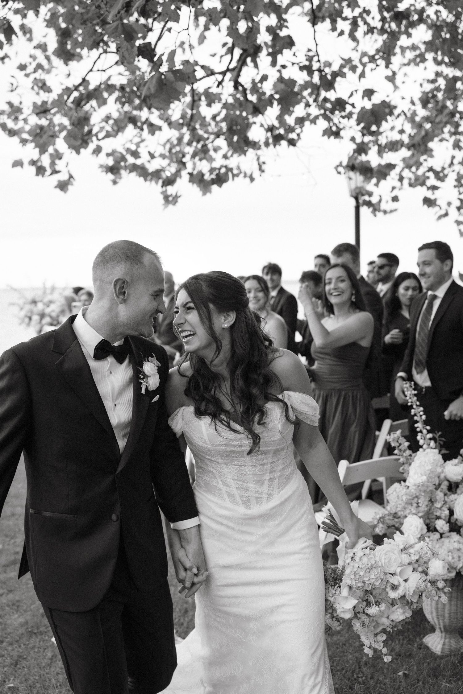 Black and white photo of a joyful bride and groom walking down the aisle after their outdoor wedding ceremony.