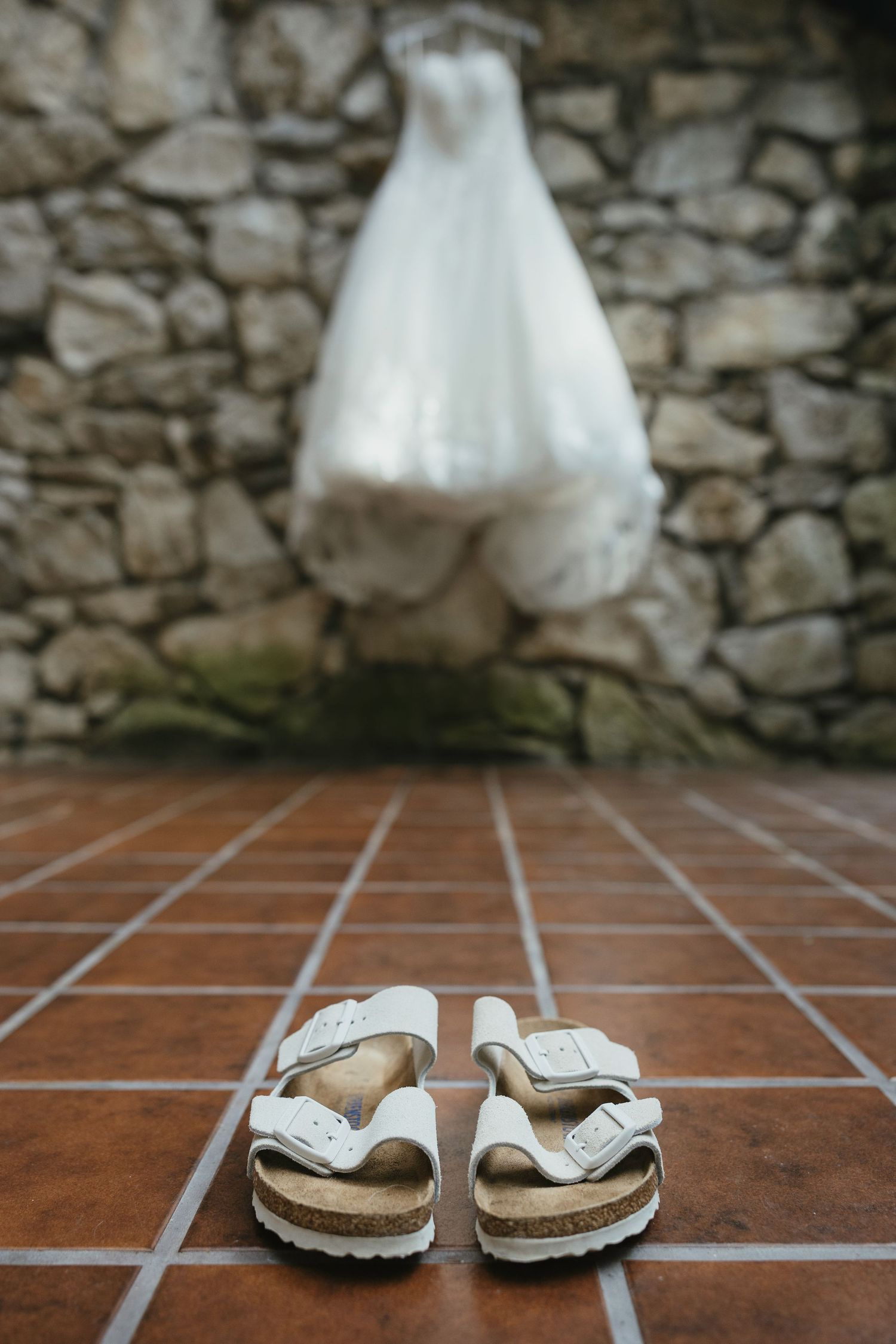 White wedding shoes placed on terracotta tiles against a rustic stone wall background.