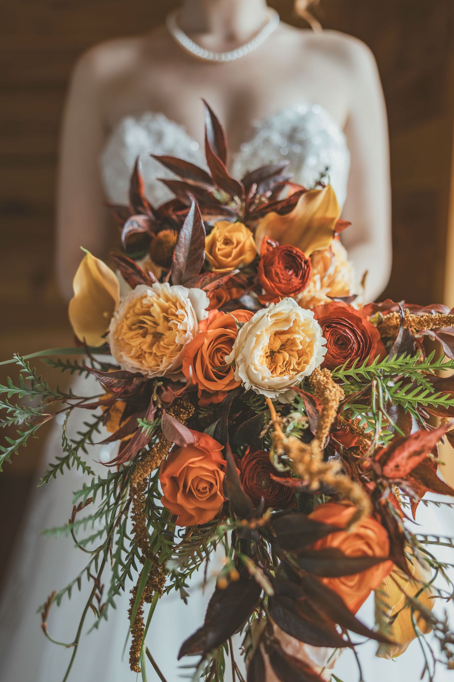 Close-up of a stunning fall wedding bouquet featuring orange roses, burgundy flowers and greenery.