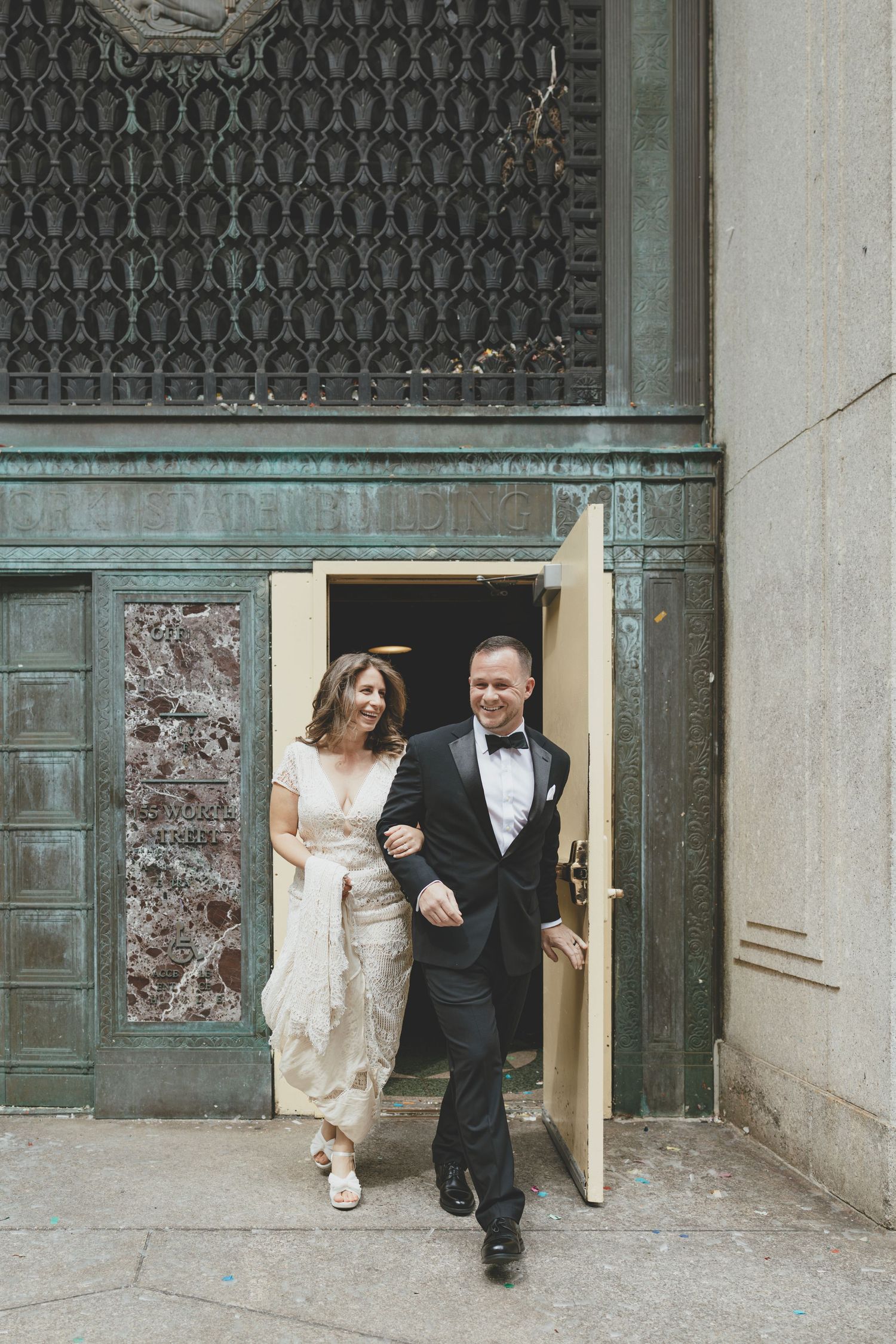A bridal couple exits through an ornate doorway with wrought iron details in a classical architectural setting.