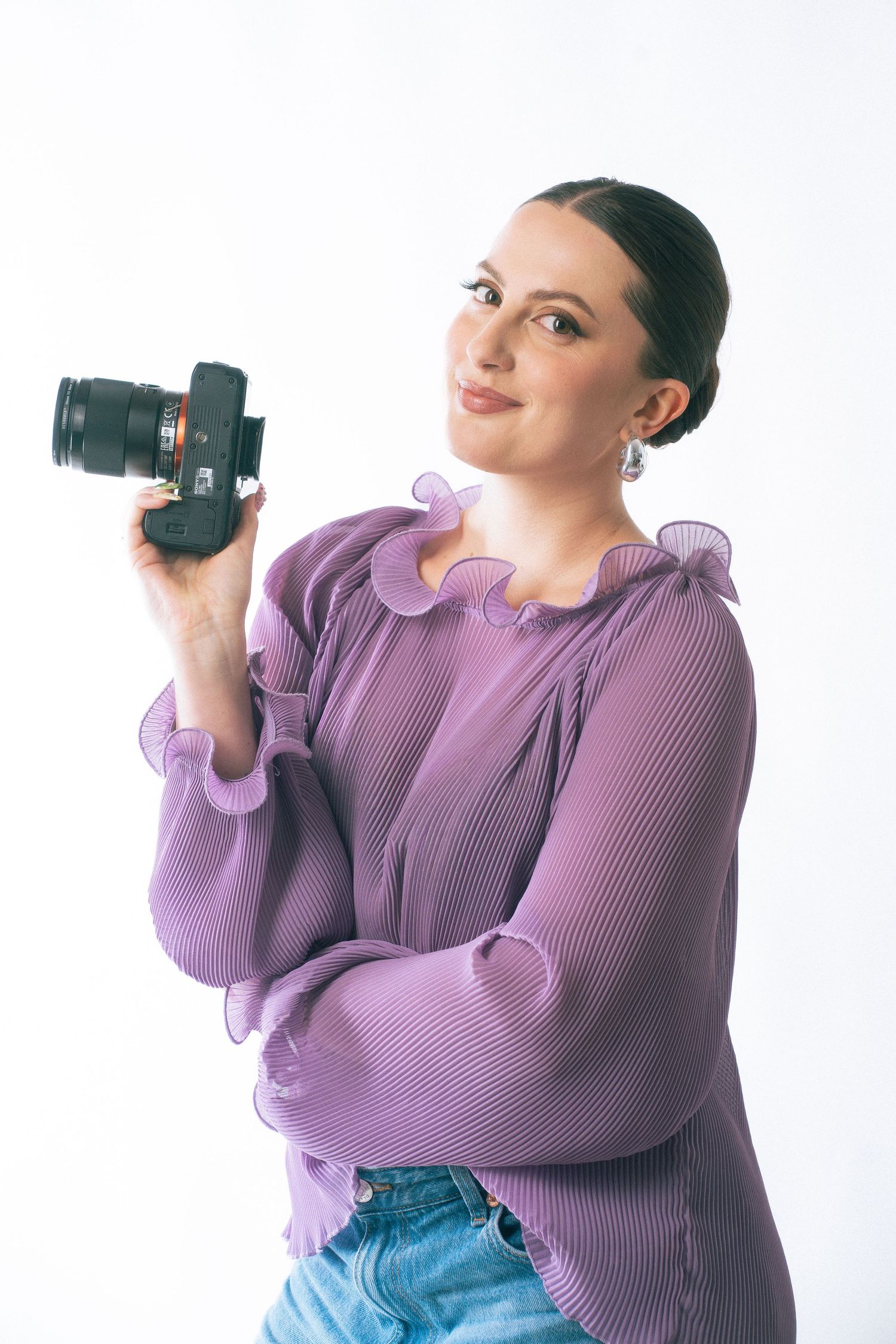 A photographer in a purple sweater and jeans poses with a camera against a white background in a series of shots.