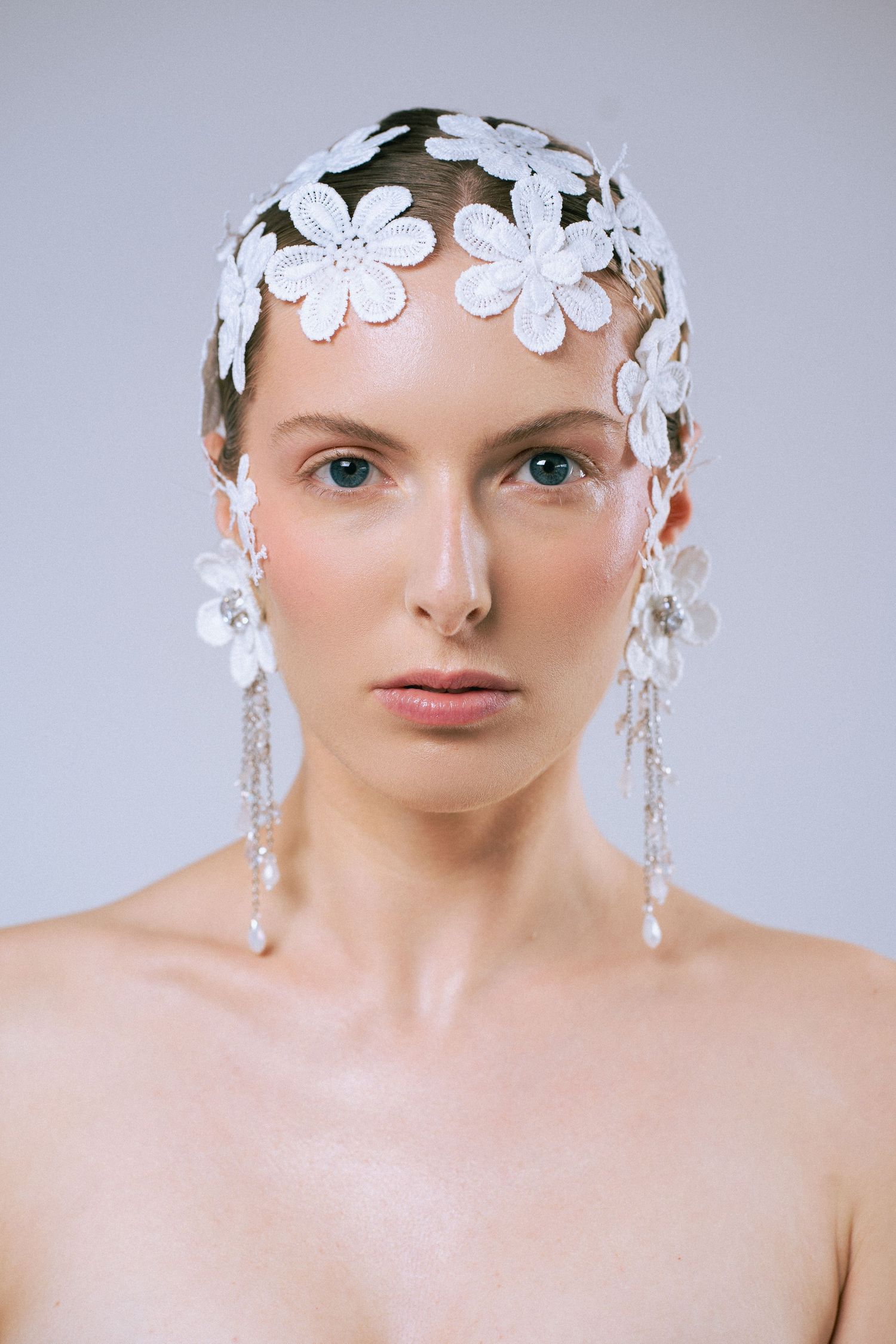 A fashion portrait featuring delicate white floral headpiece with crystal embellishments against a light gray background.