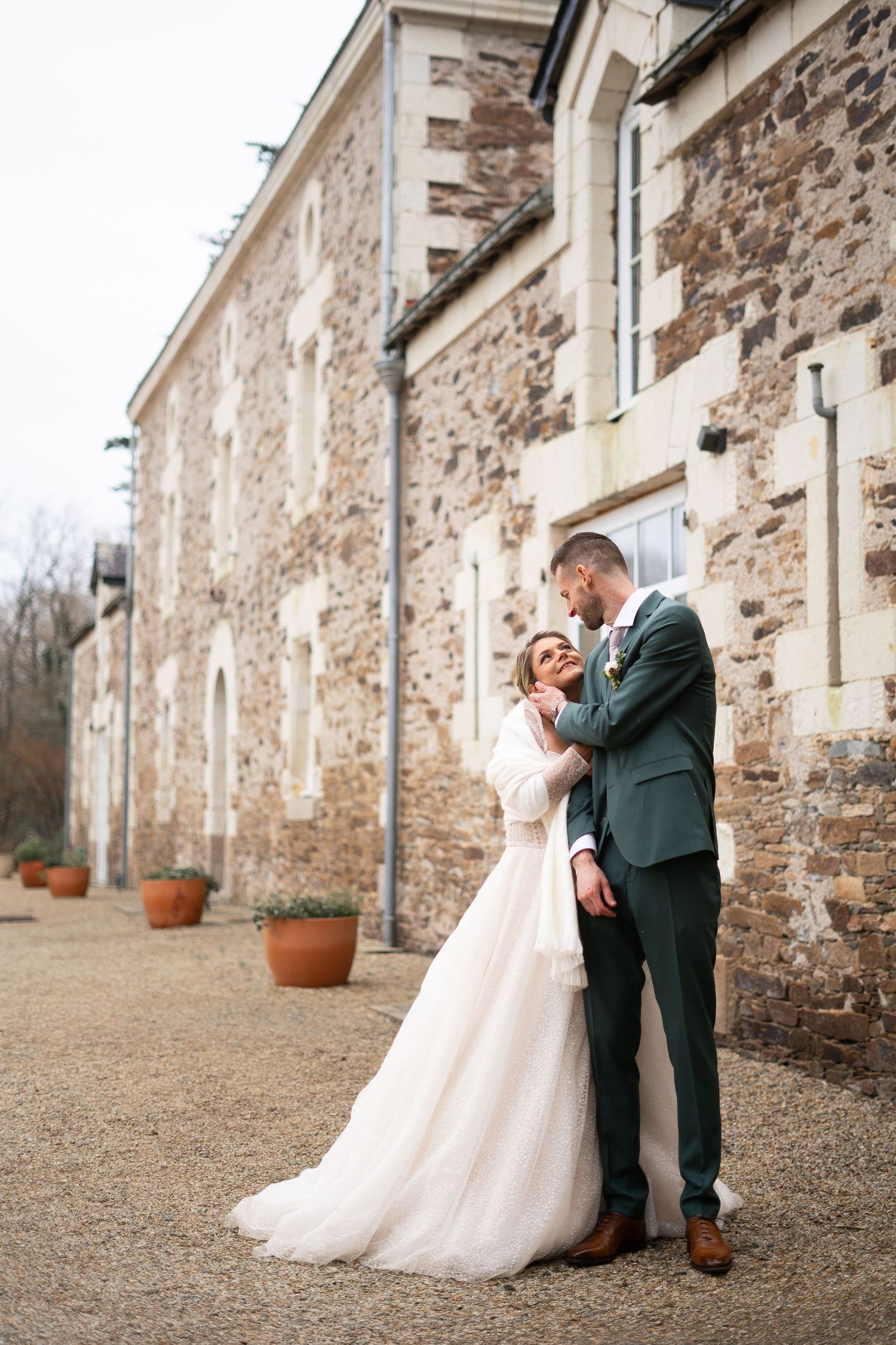 Romantic portrait of newlyweds embracing against a rustic stone wall backdrop.
