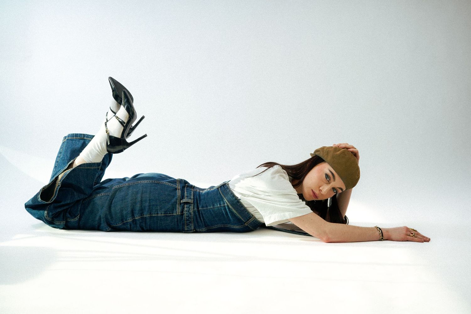 Fashion shot of model lying on floor wearing jeans and high heels against white background.