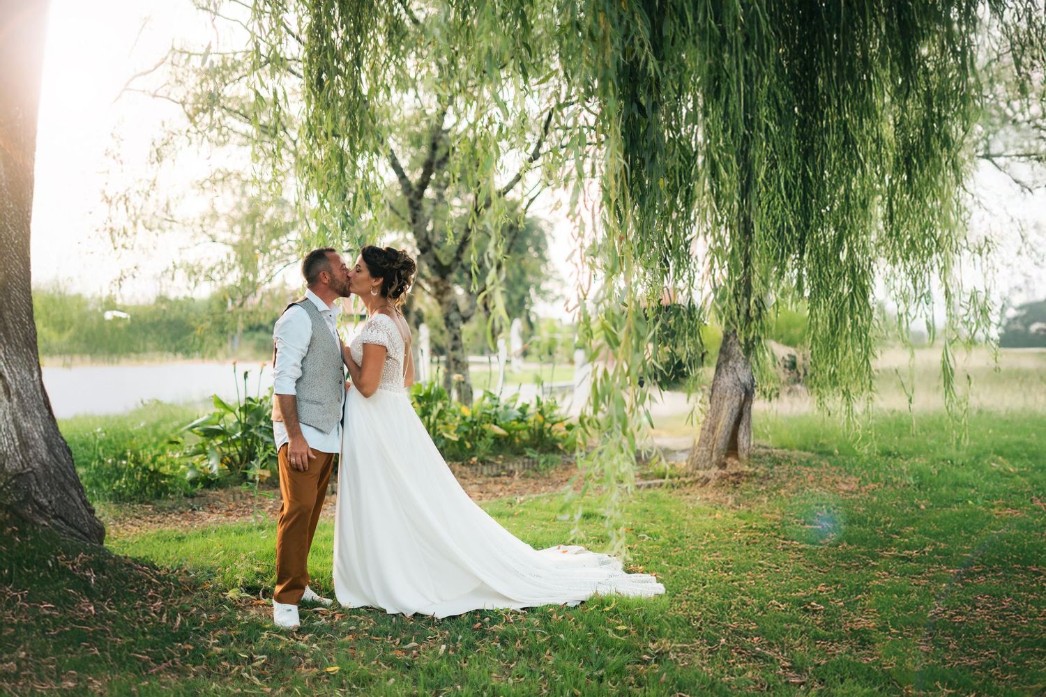 Romantic couple shares tender moments under weeping willow trees in an enchanting garden setting during golden hour.