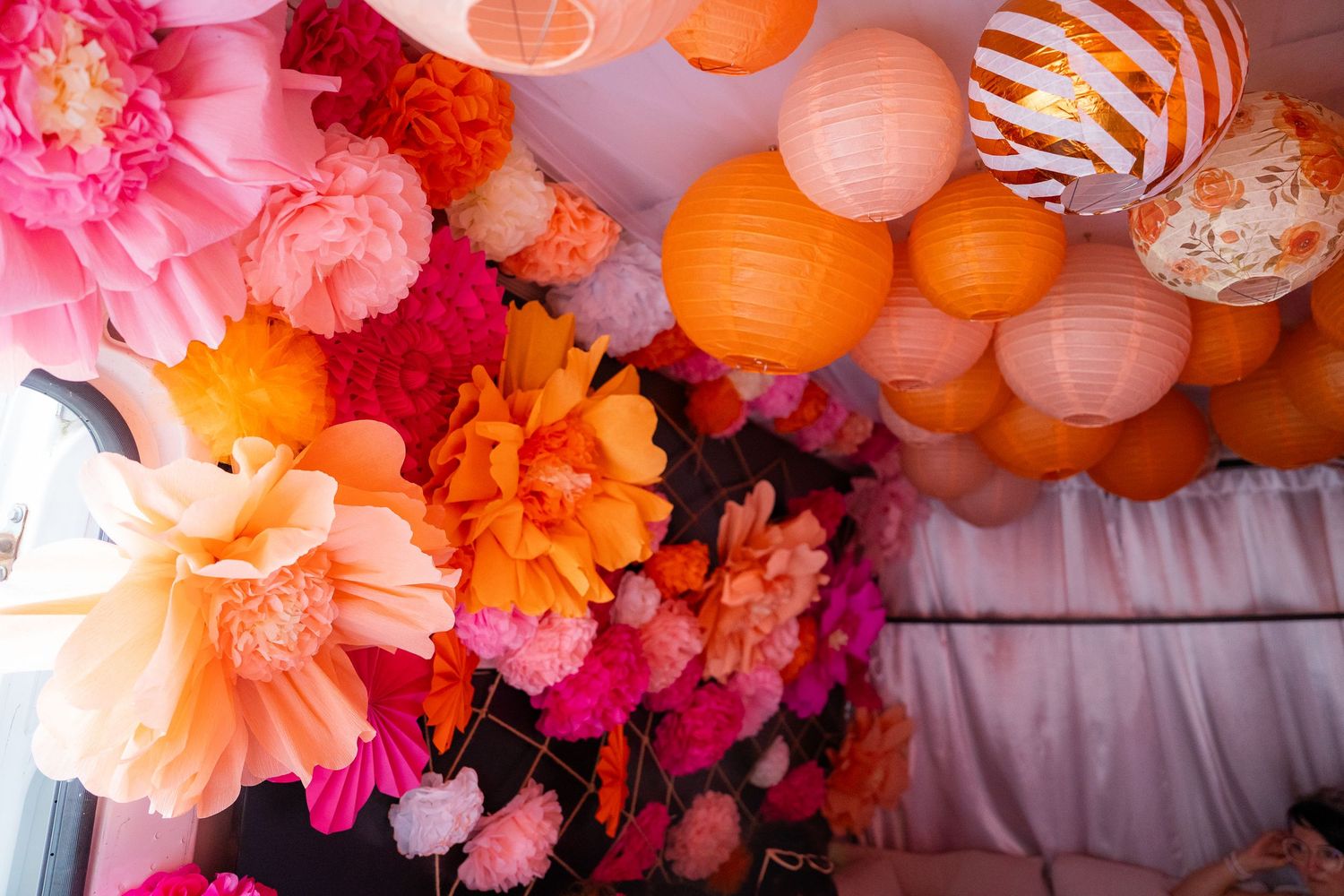Colorful paper lanterns and tissue pom poms in pink and orange create a festive party ceiling decoration.