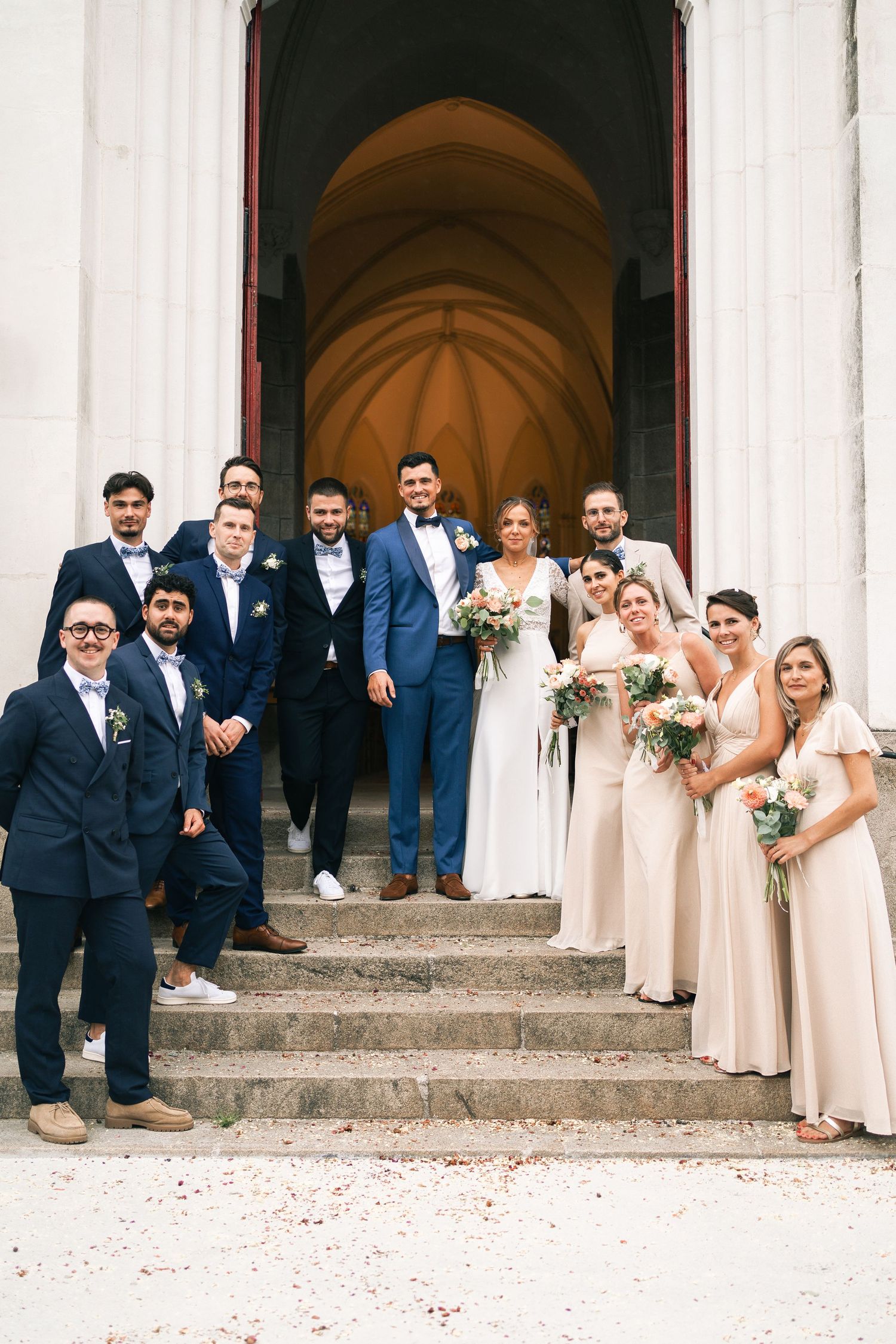 Wedding party in navy blue and beige attire poses on stone church steps in three different candid groupings.