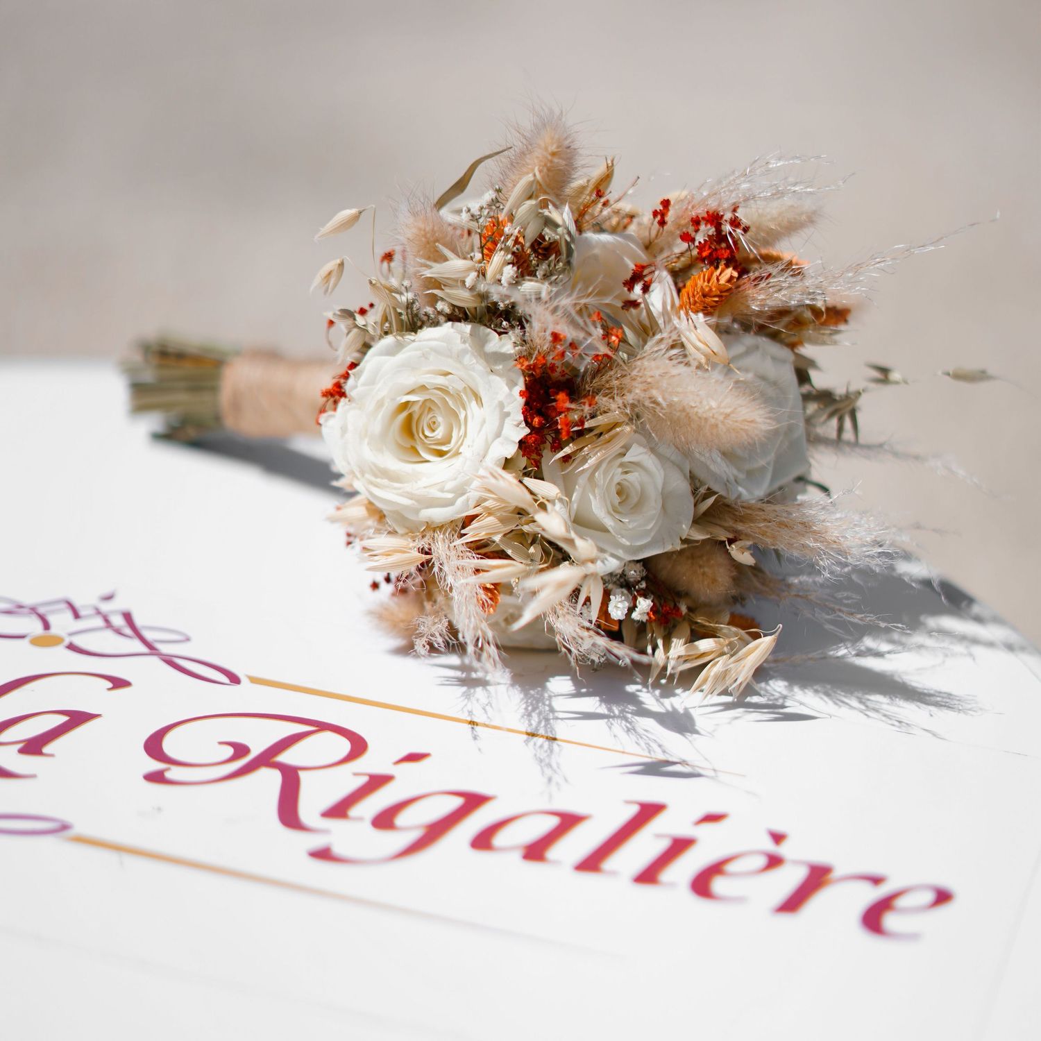 Elegant wedding bouquet with white roses and dried flowers casting shadow on text.