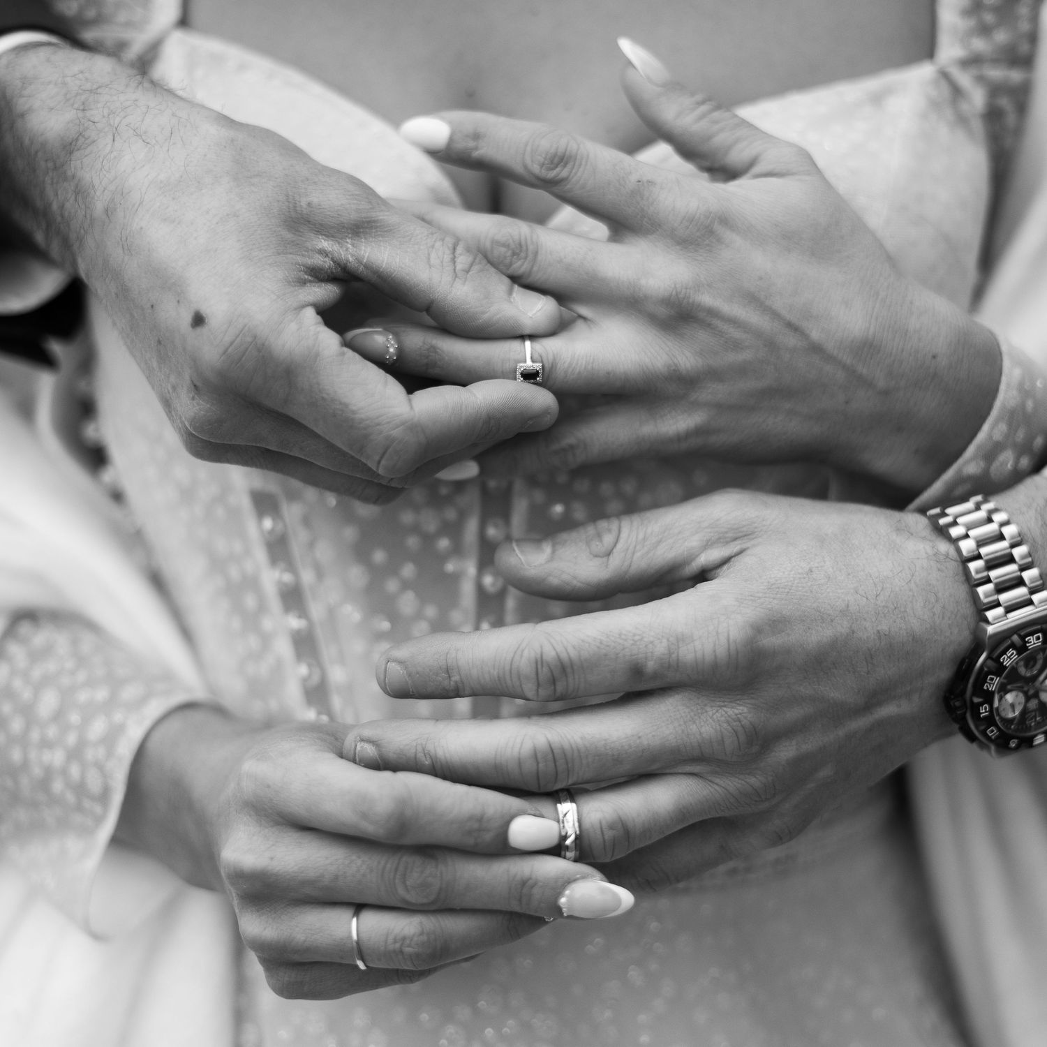 Black and white close-up of multiple hands displaying wedding rings and intimate touches.