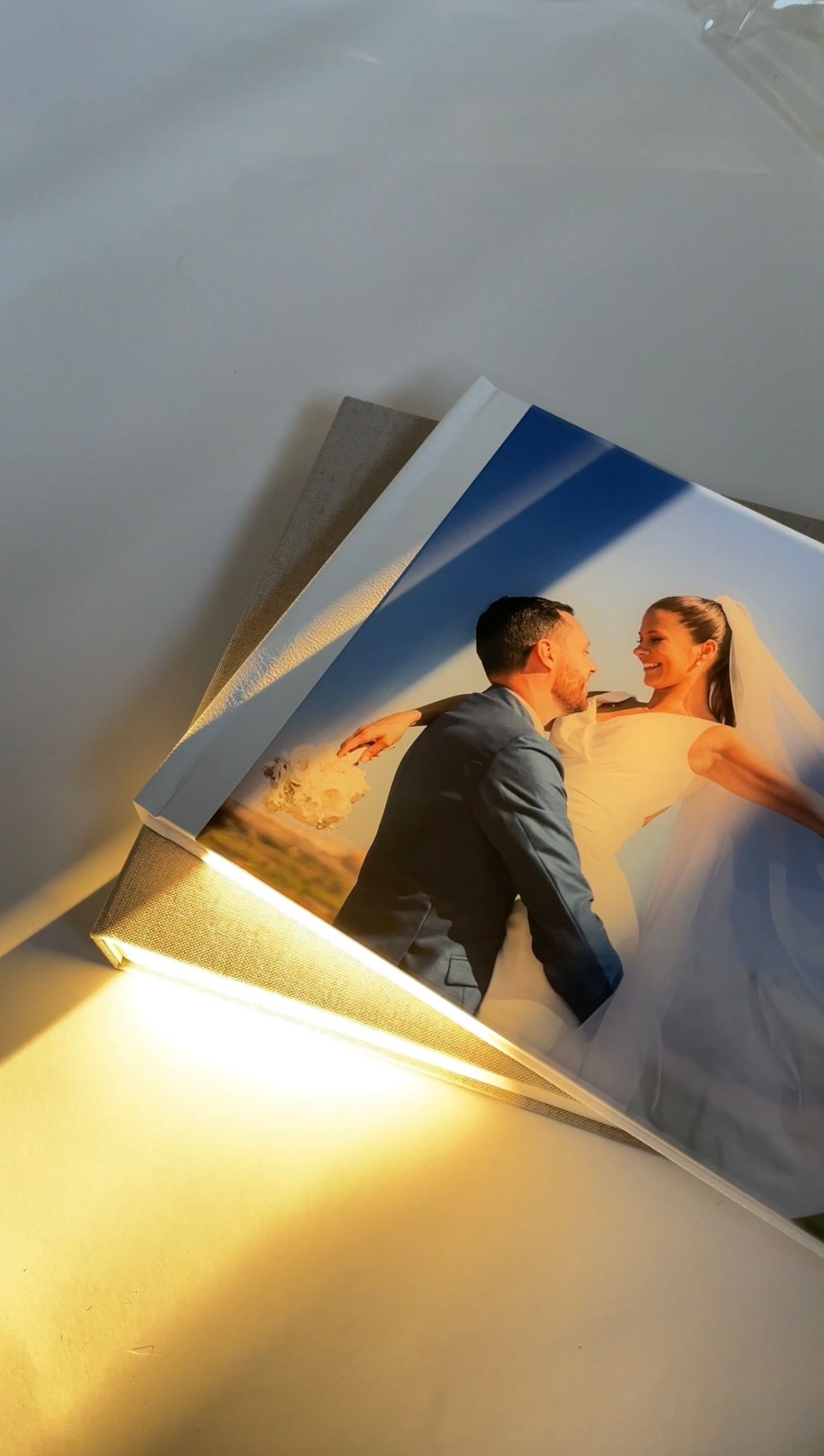 Wedding photographs spread out on a white surface with warm lighting illuminating a romantic couple's portrait.