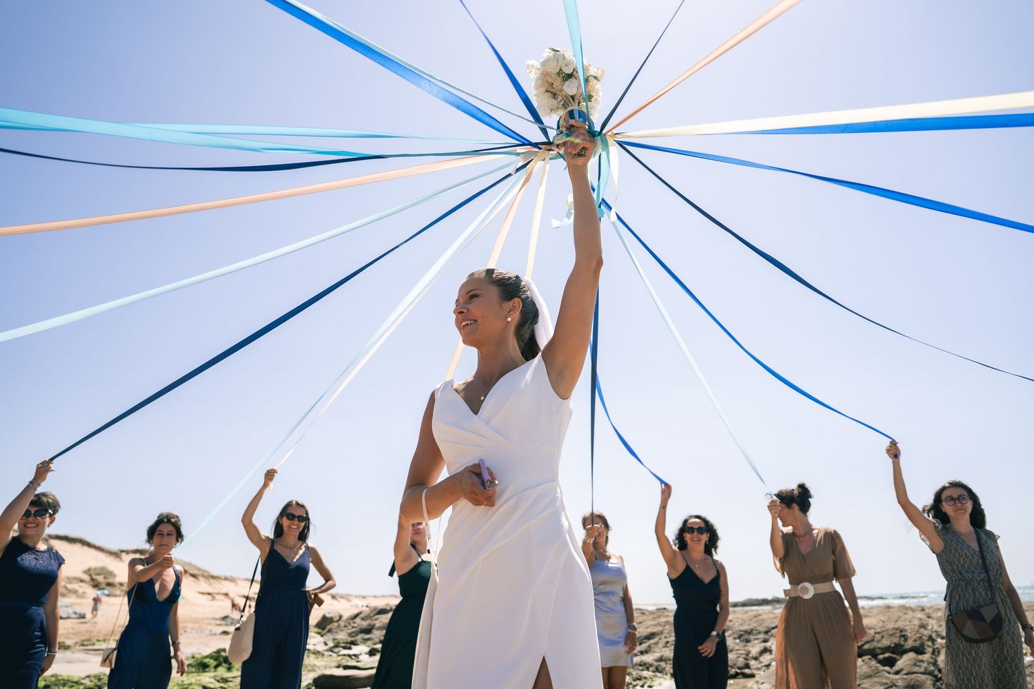 A group of people stand with raised arms under a ceremony canopy, participating in what appears to be a wedding ritual.