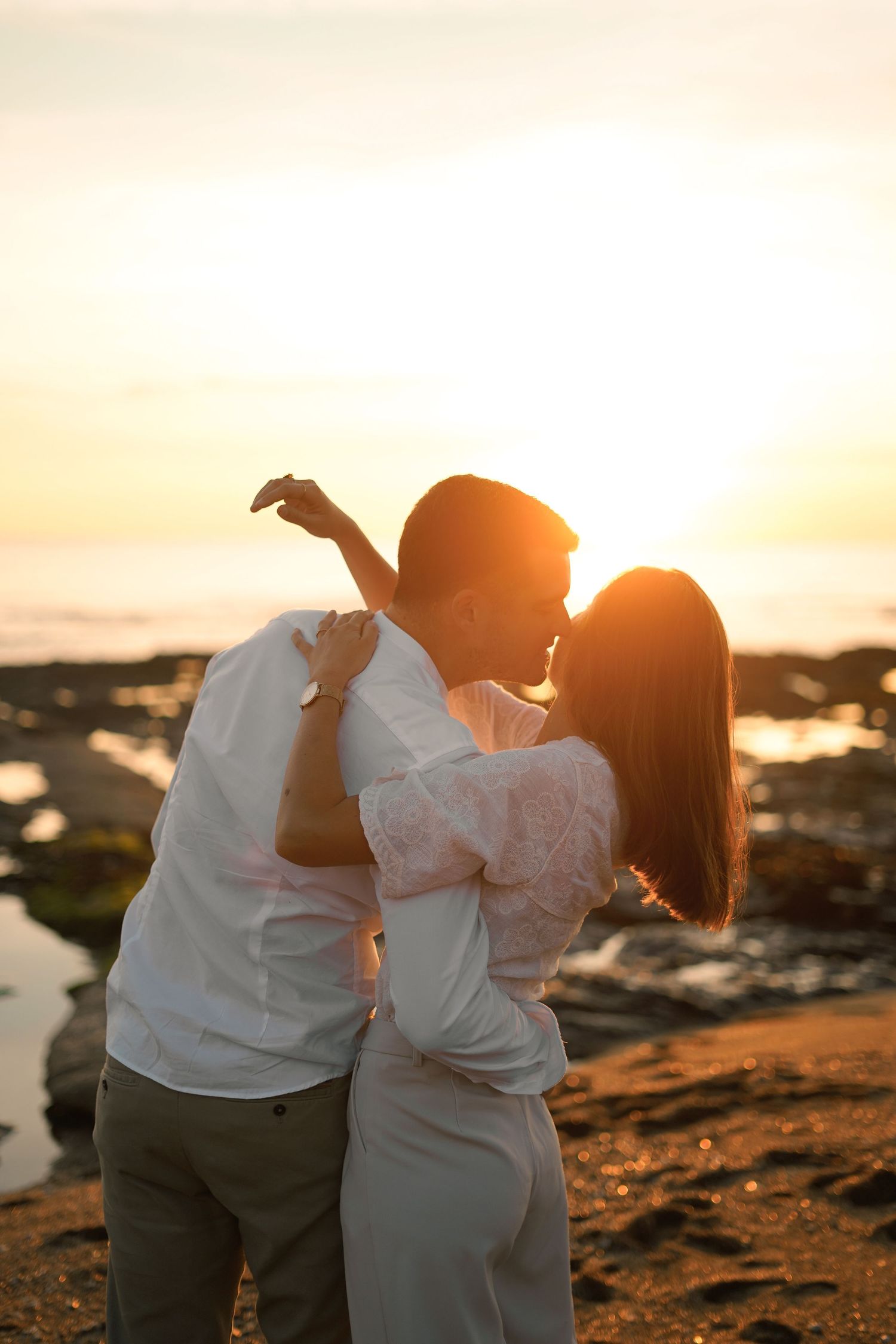 Romantic silhouette of couple embracing at sunset against coastal landscape.