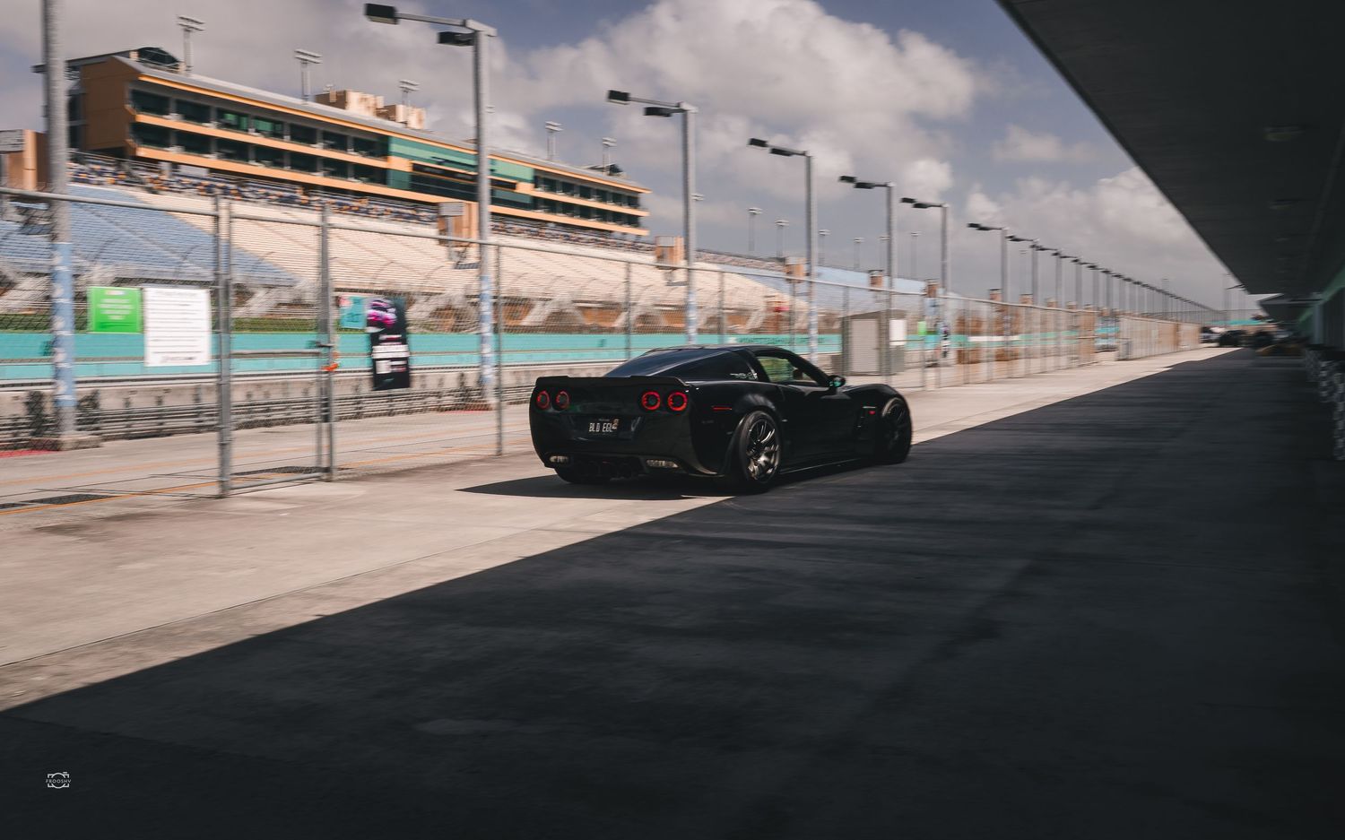 Black sports car parked on concrete road with parking structure and cloudy sky in background.