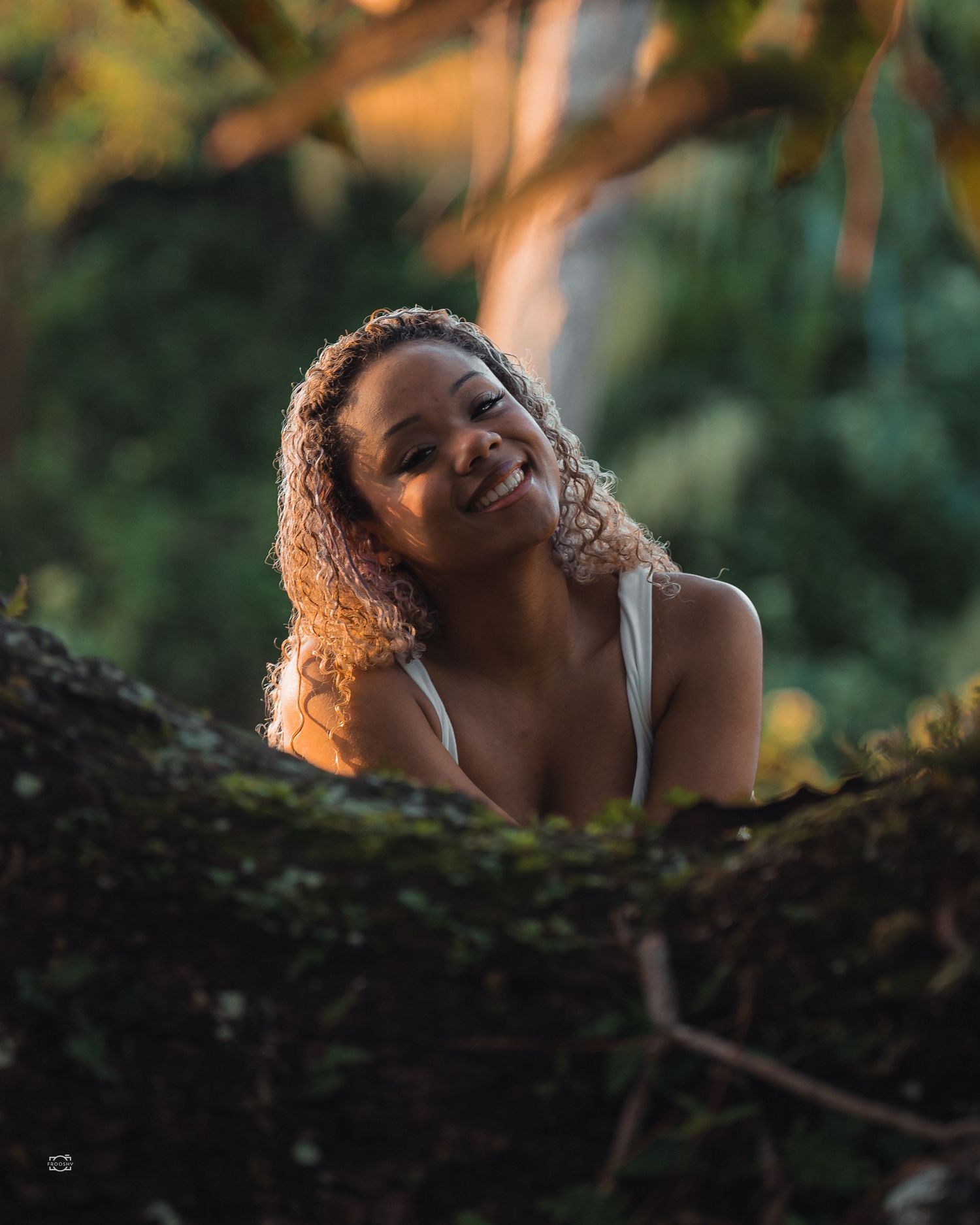 A person rests their head against a mossy tree trunk at golden hour, creating a dreamy outdoor portrait series.