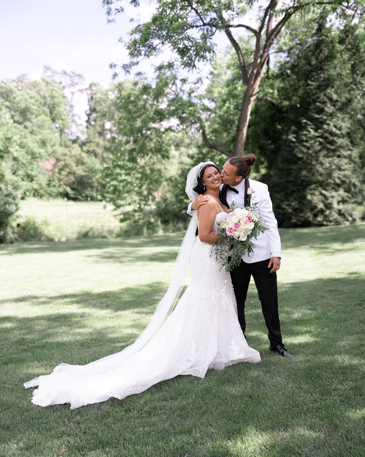 A couple shares a romantic moment on their wedding day in a sunlit garden setting with lush greenery.