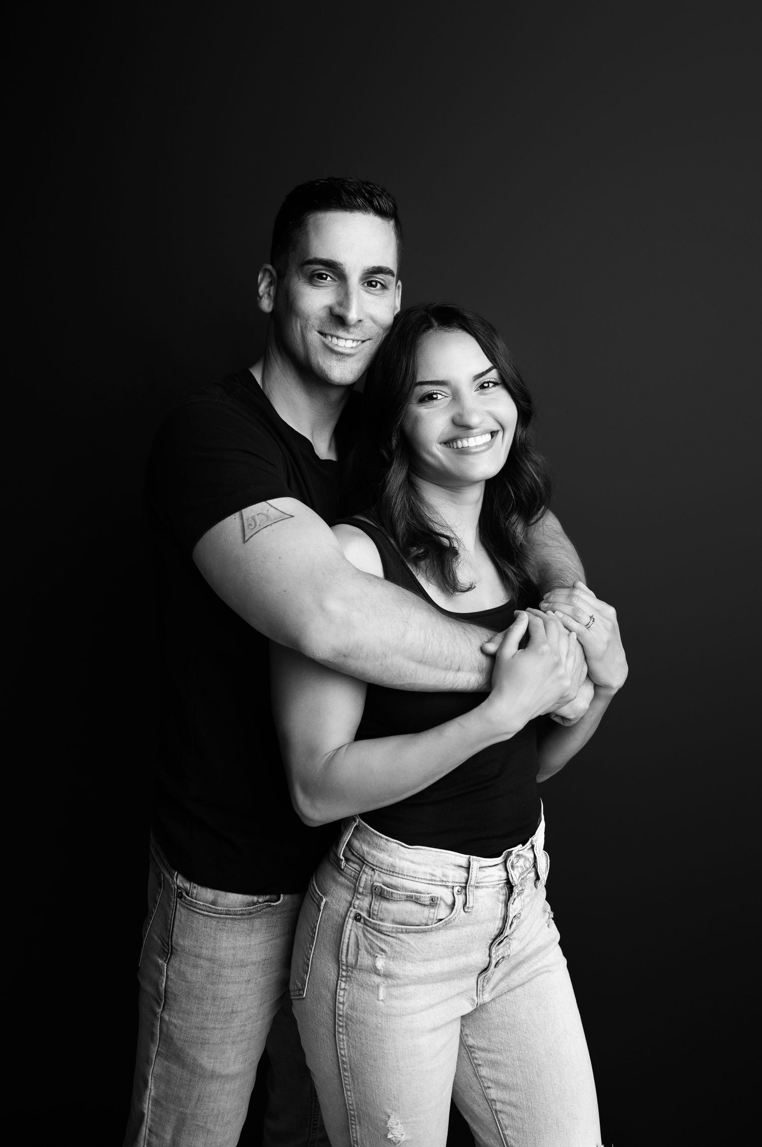 Artistic black and white photo series showing tender embrace between two people wearing jeans against dark background.