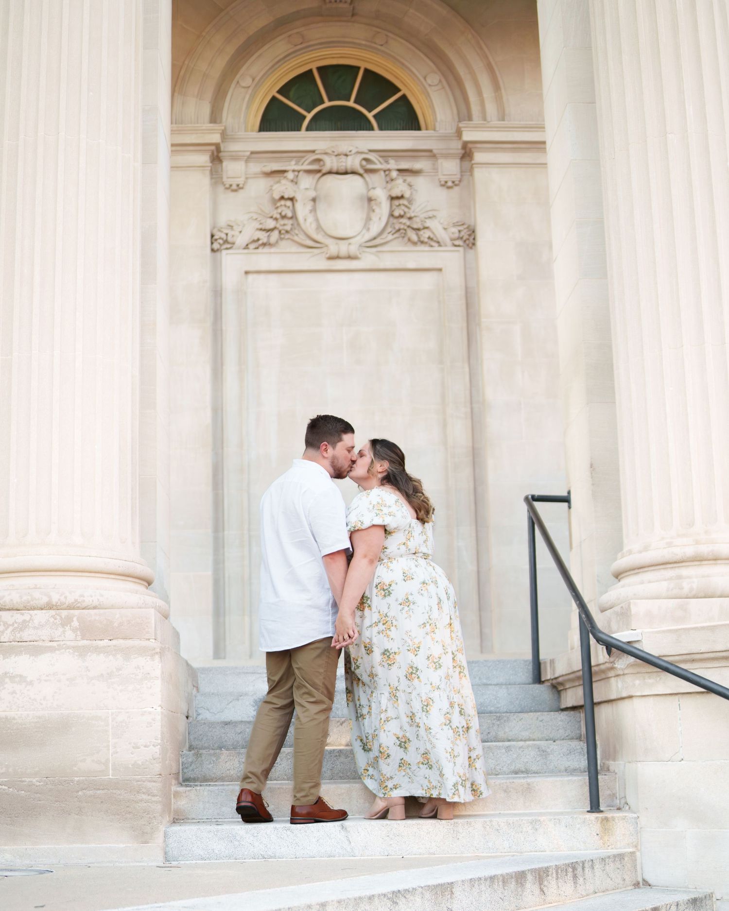 Couple shares romantic moments in front of elegant white columns and arched windows of a historic building.