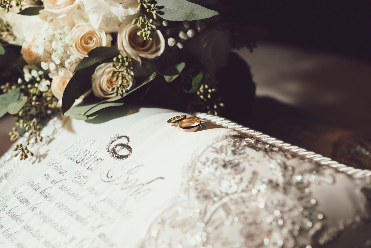 Wedding rings and delicate floral decorations rest on handwritten paper with elegant calligraphy.