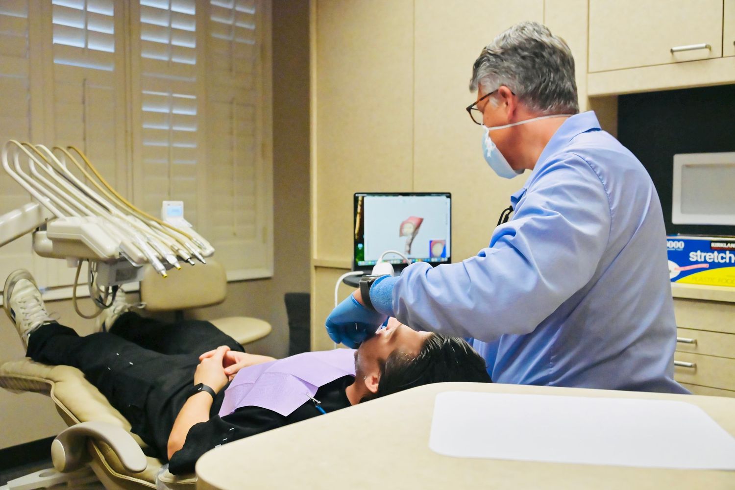 Dentist performing a dental examination on a reclined patient in a modern dental office chair.