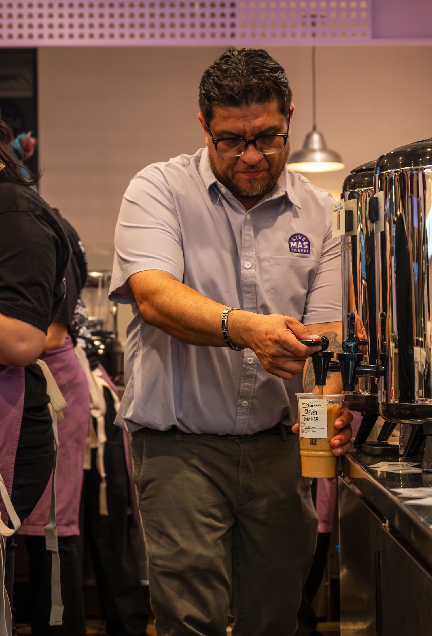 Taco Bell manager in a blue shirt preparing a drink at the beverage station.