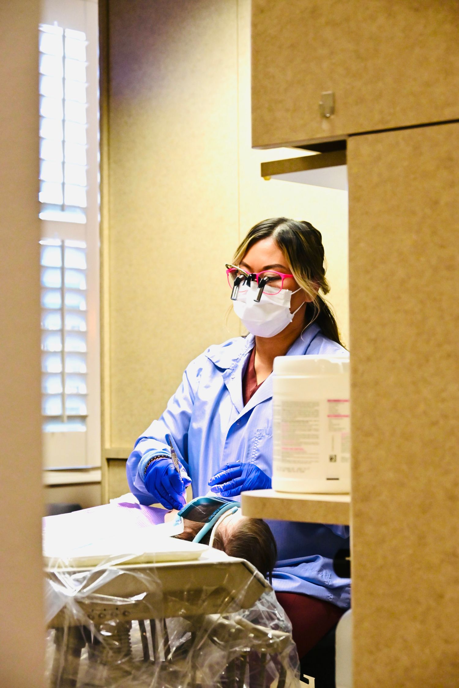 Female dental assistant in blue scrubs and red glasses prepares instruments at sterilization station.