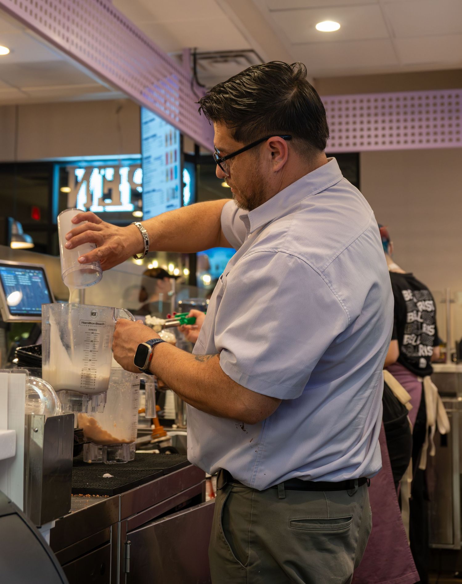Taco Bell staff member pouring ingredients into a blender at the food preparation counter.