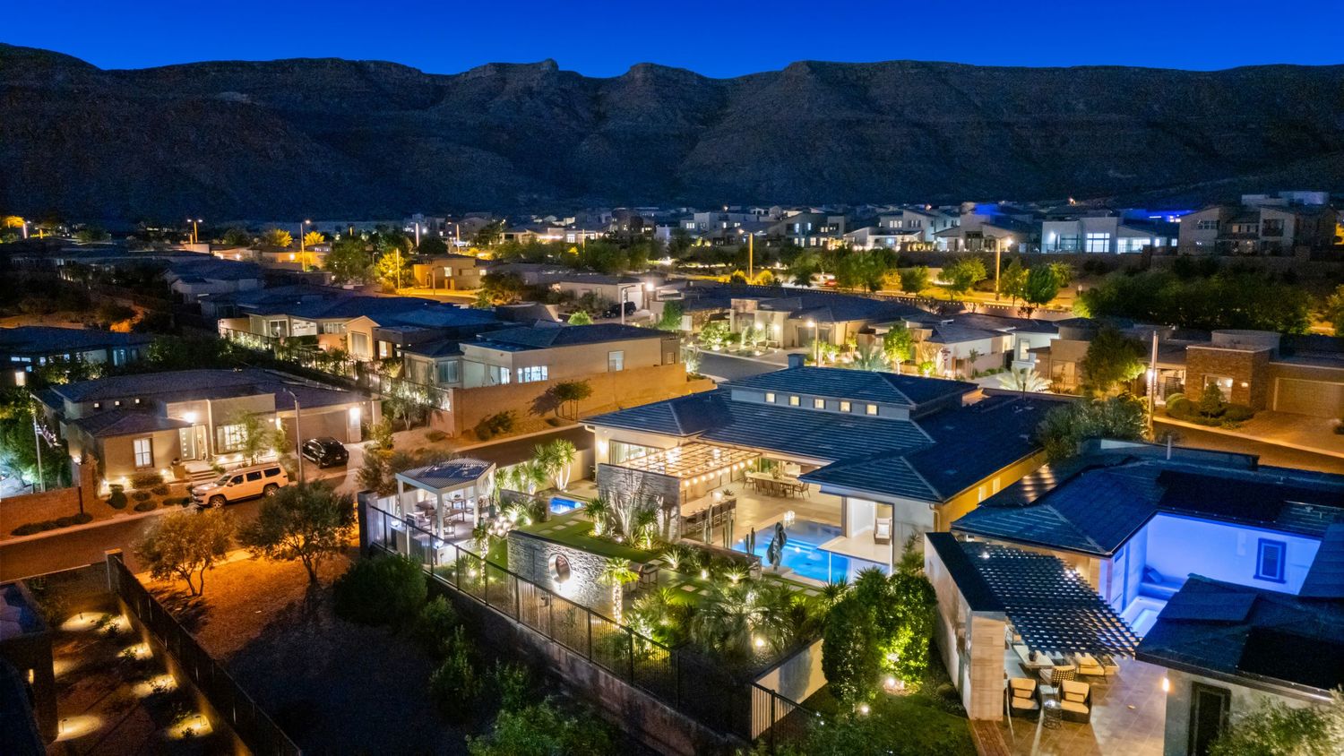 Aerial twilight view of a luxury resort with illuminated villas, pool, and mountain backdrop at dusk.