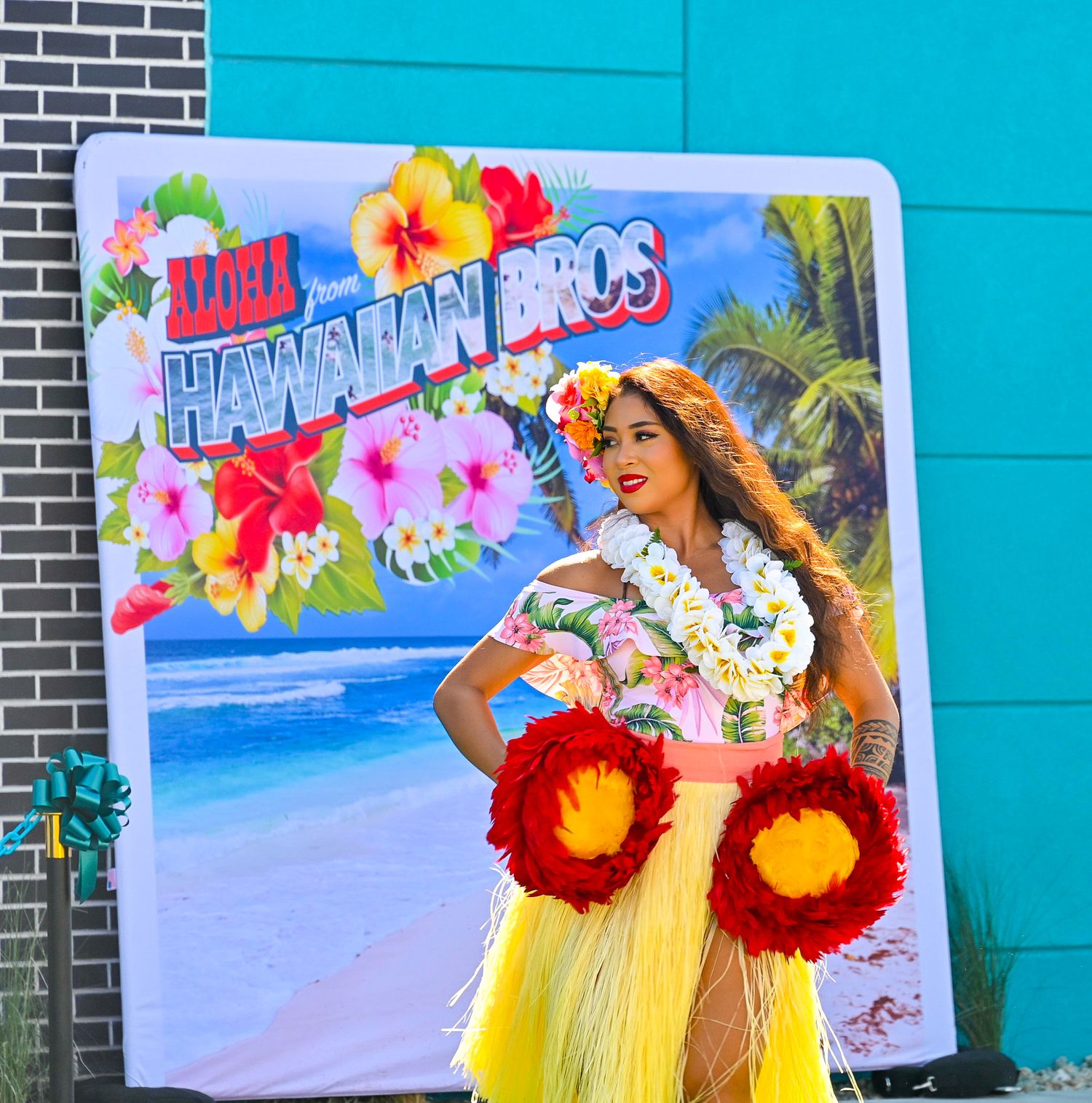 Woman in Hawaiian hula costume posing in front of Hawaiian Bros restaurant promotional sign.
