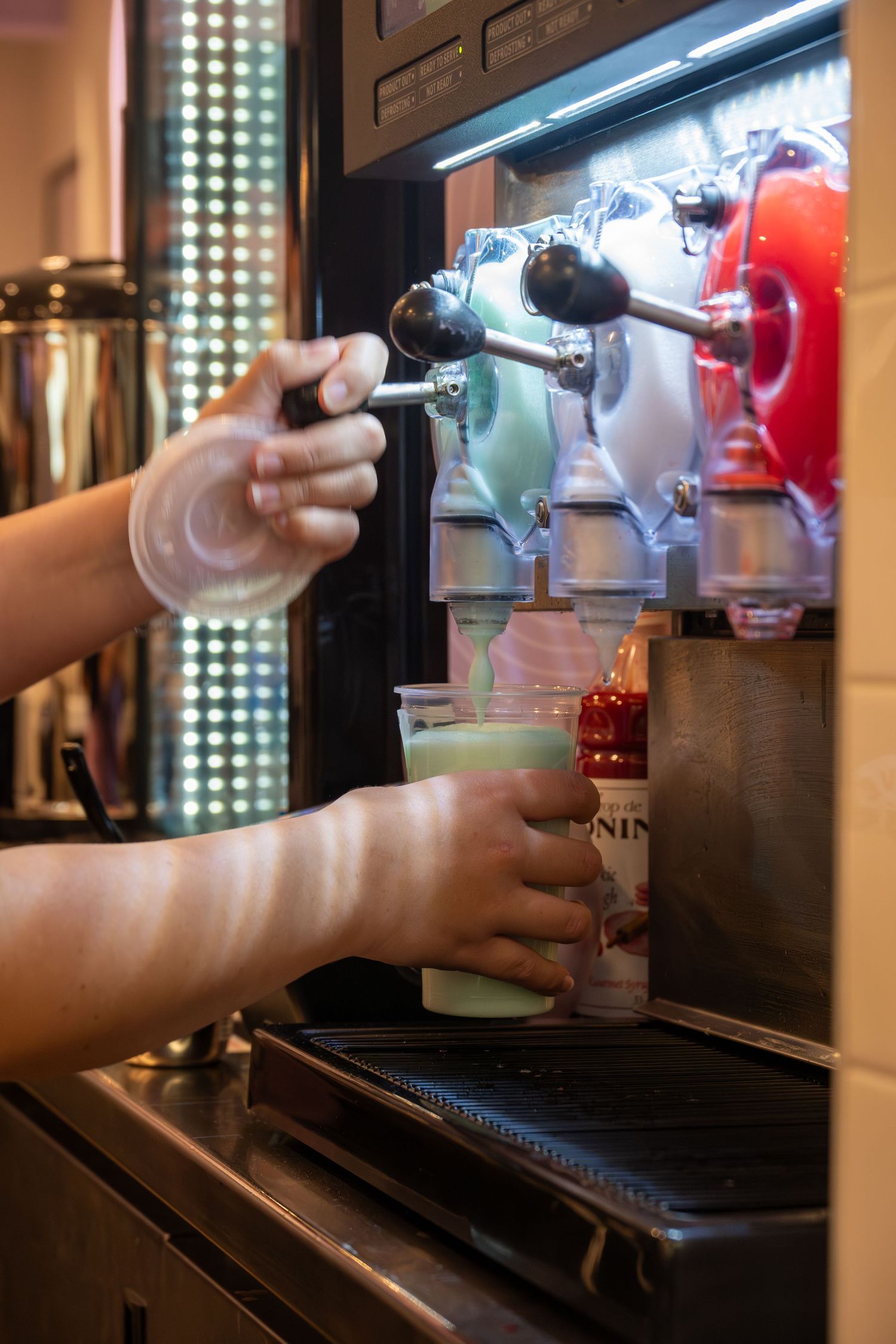 Taco Bell employee dispensing a green frozen drink from a colorful slushie machine.
