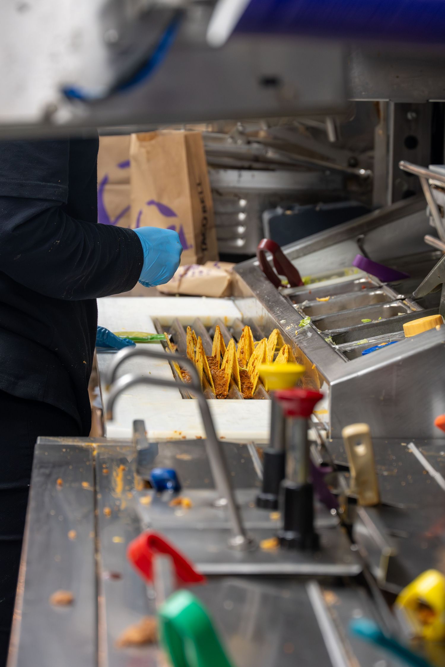 Food service worker assembling crispy tacos in holders on a stainless steel commercial kitchen line.