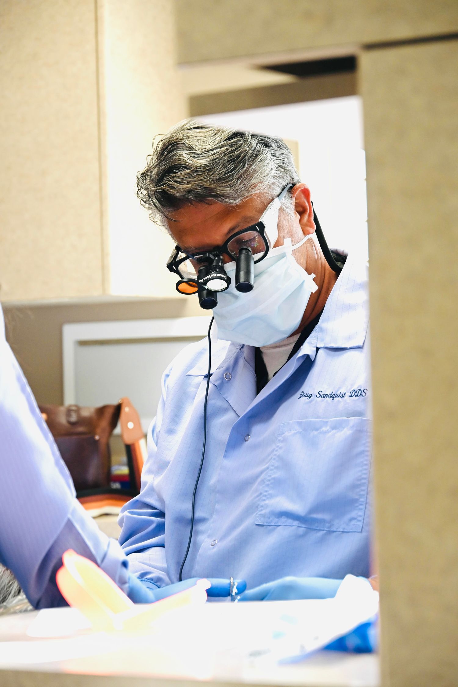 Dentist wearing magnifying loupes and surgical mask examines patient in modern dental office.